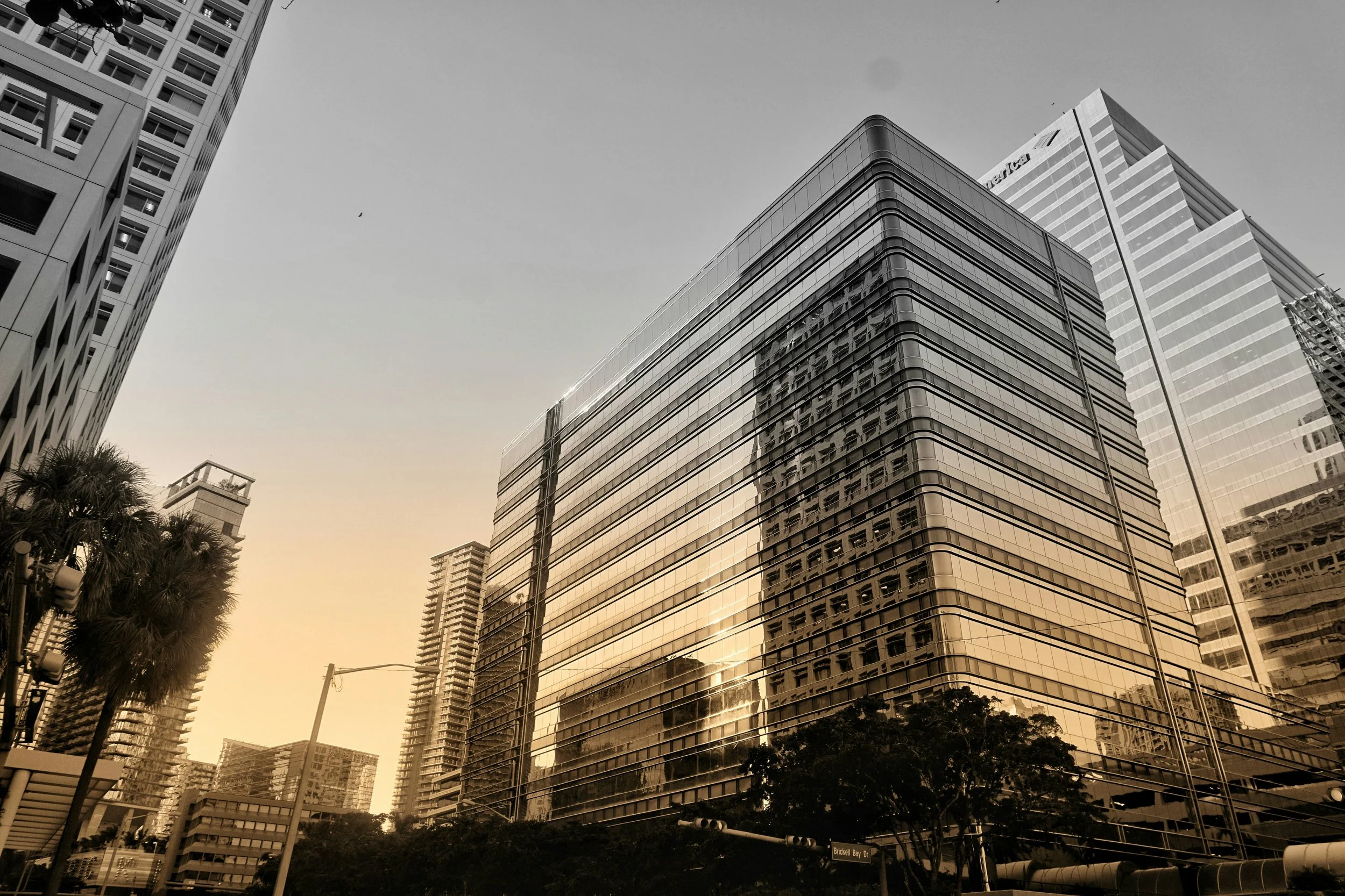 Reflections of surrounding skyscrapers on the glass facade of a modern office building in an urban cityscape at sunset.