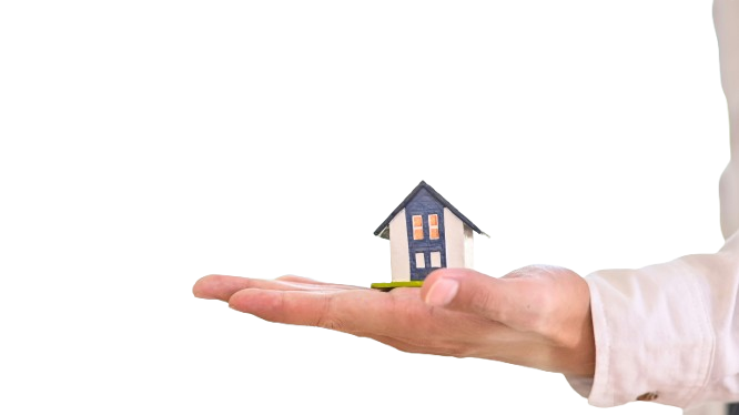 A person's hand holding a small model house, with a person in business attire in the background.