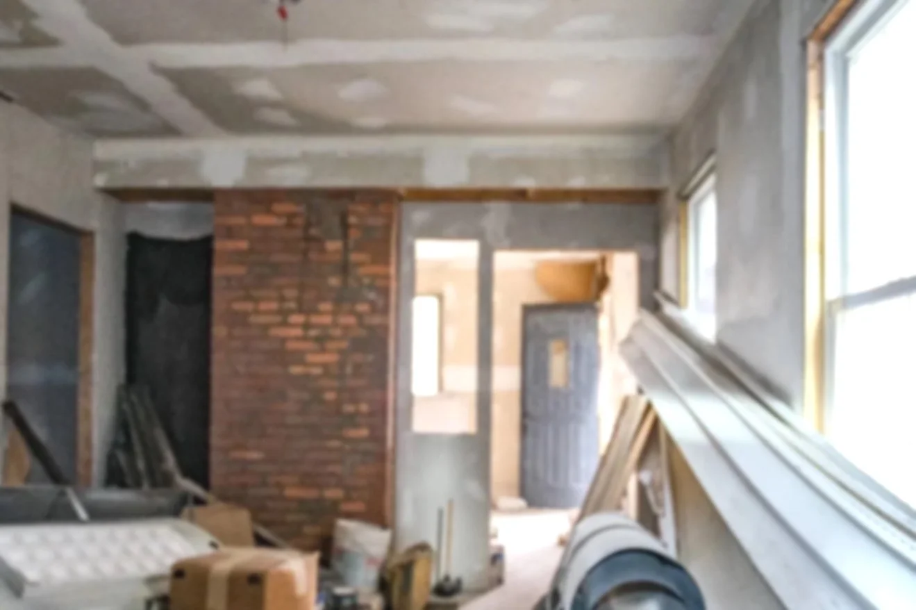 Interior of a room under construction, with a brick wall, unfinished walls, and construction materials scattered around.