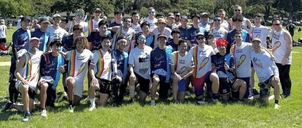 Group of young adults and teenagers outdoors on a sunny day, posing for a photo on grass.