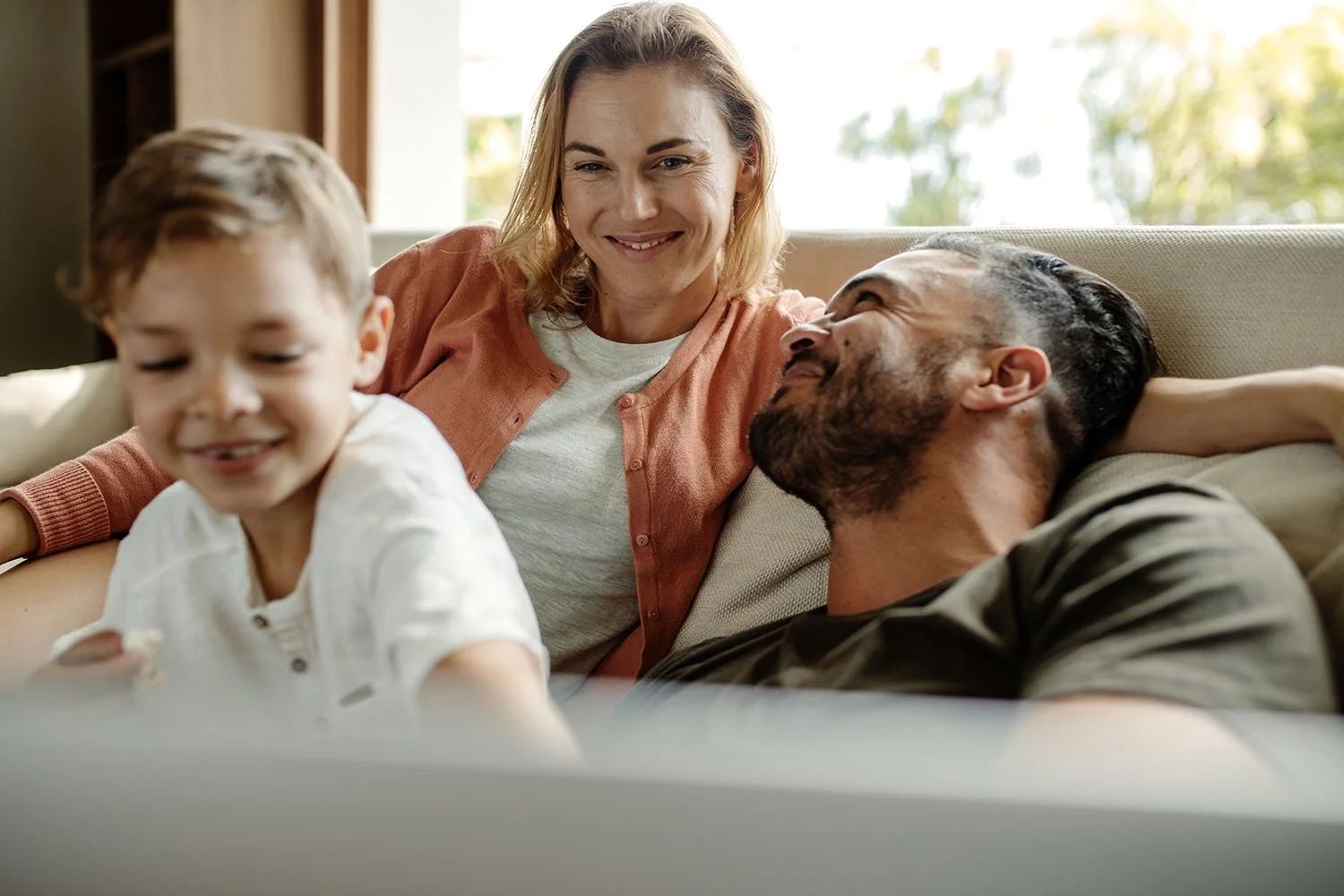 Family owned business owners - A woman, a young boy, and a man relaxing together on a couch, smiling and enjoying each other's company.