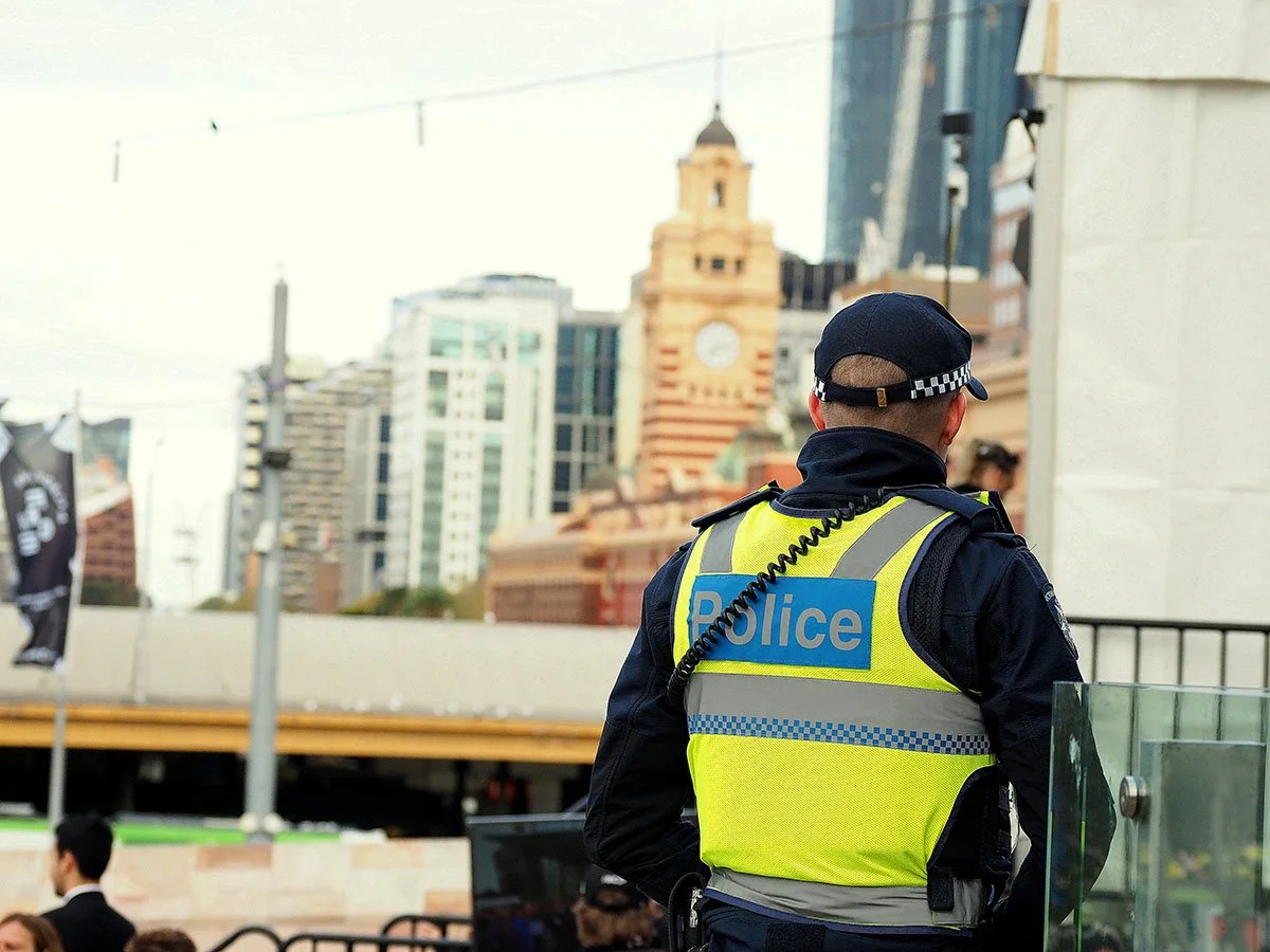 A police officer in a yellow vest, or a emergency service worker, with Melbourne cityscape in the background.