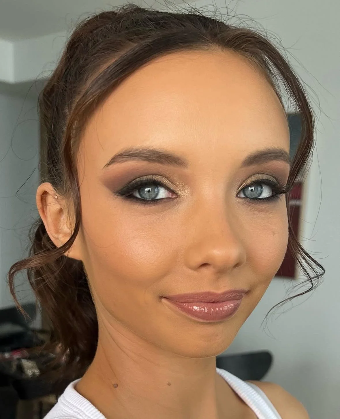 Close-up of a woman with makeup, including smoky eyeshadow, blush, and lipstick, smiling softly.
