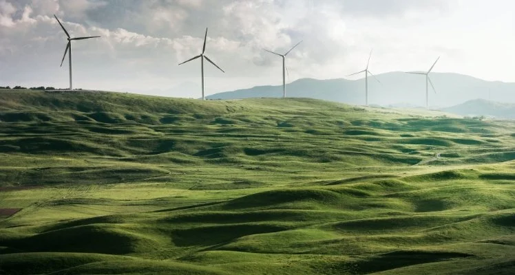 Rolling green hills with wind turbines on the horizon under cloudy sky.