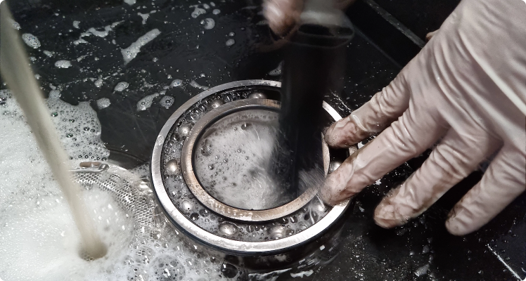Person wearing gloves cleaning and inspecting a bearing in a workshop or garage.