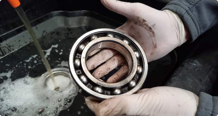 Person wearing gloves washing a large ball bearing in soapy water.