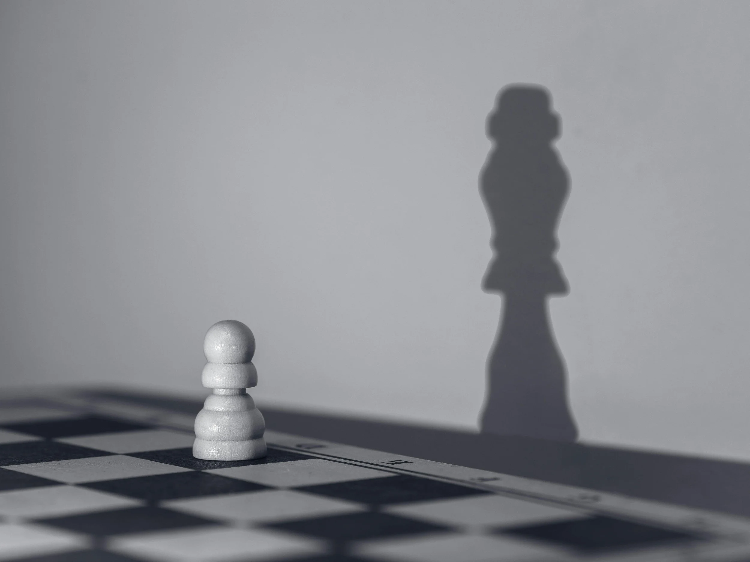 A white pawn chess piece casting a shadow that resembles a king on a chessboard.
