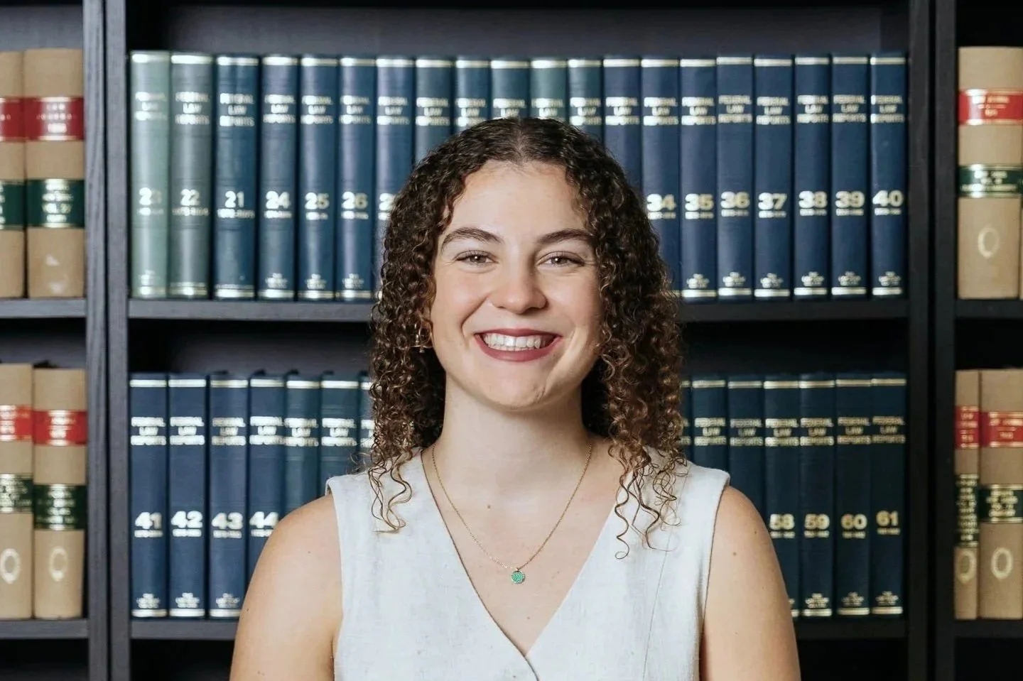 A woman with curly hair smiling in front of a bookshelf filled with legal books.