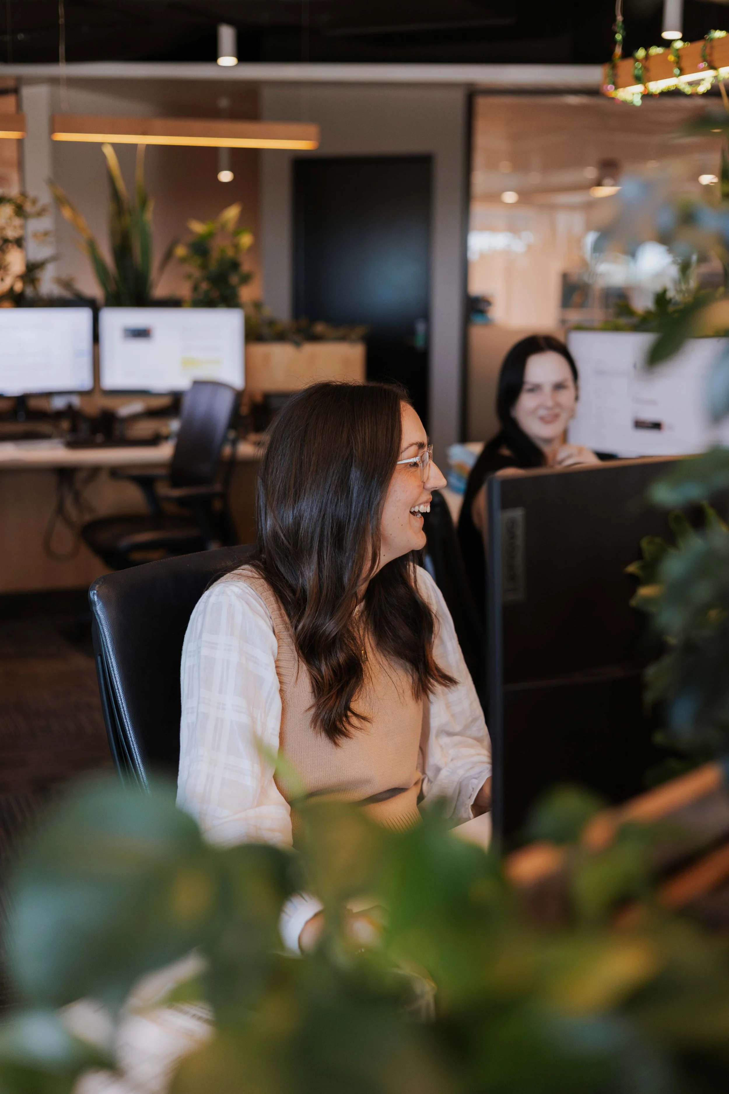 Female lawyer sitting at a desk, laughing, with another female coworker smiling in the background