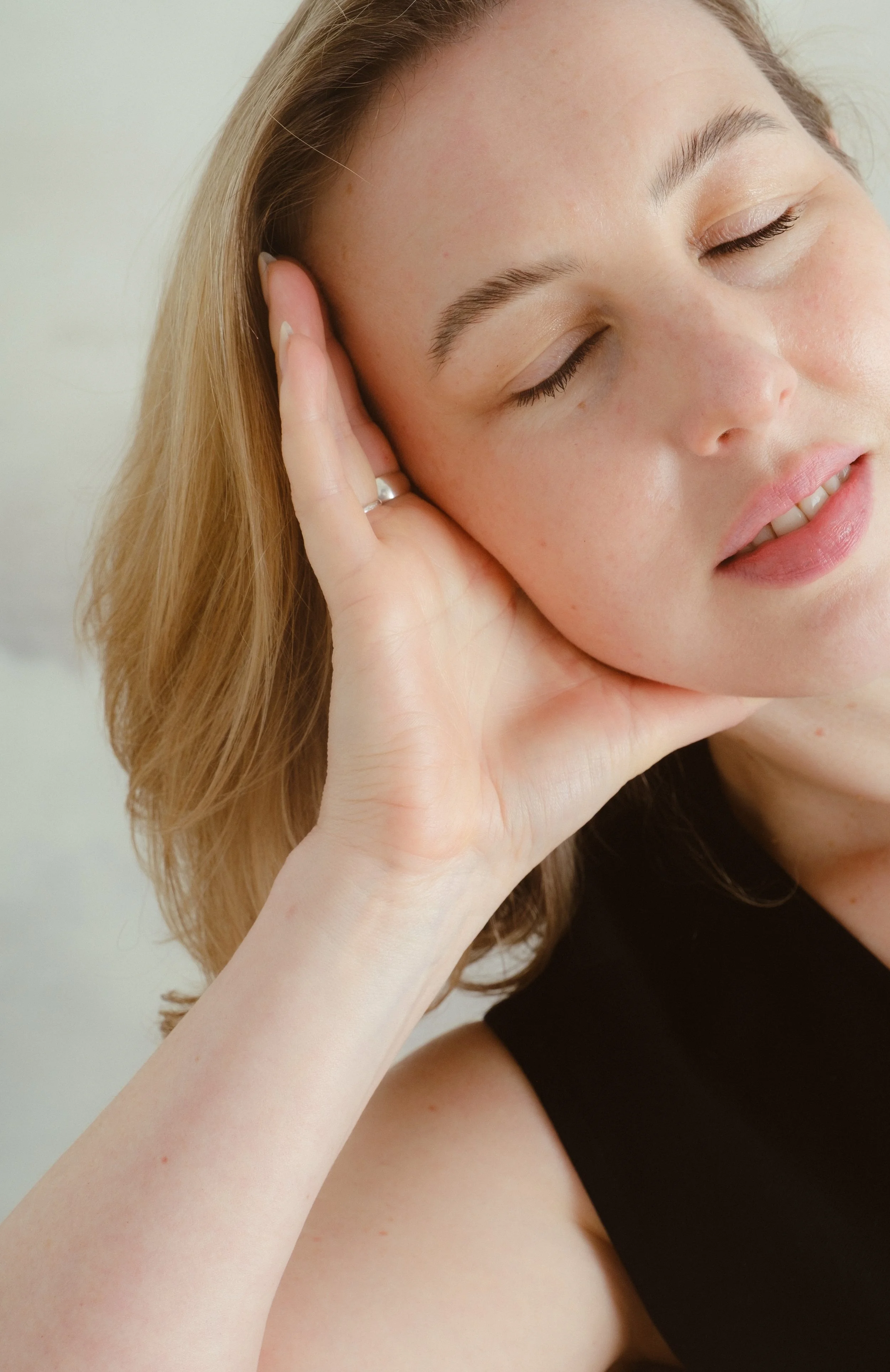 Close-up of a woman with fair skin and light brown hair, resting her cheek on her hand with her eyes closed.