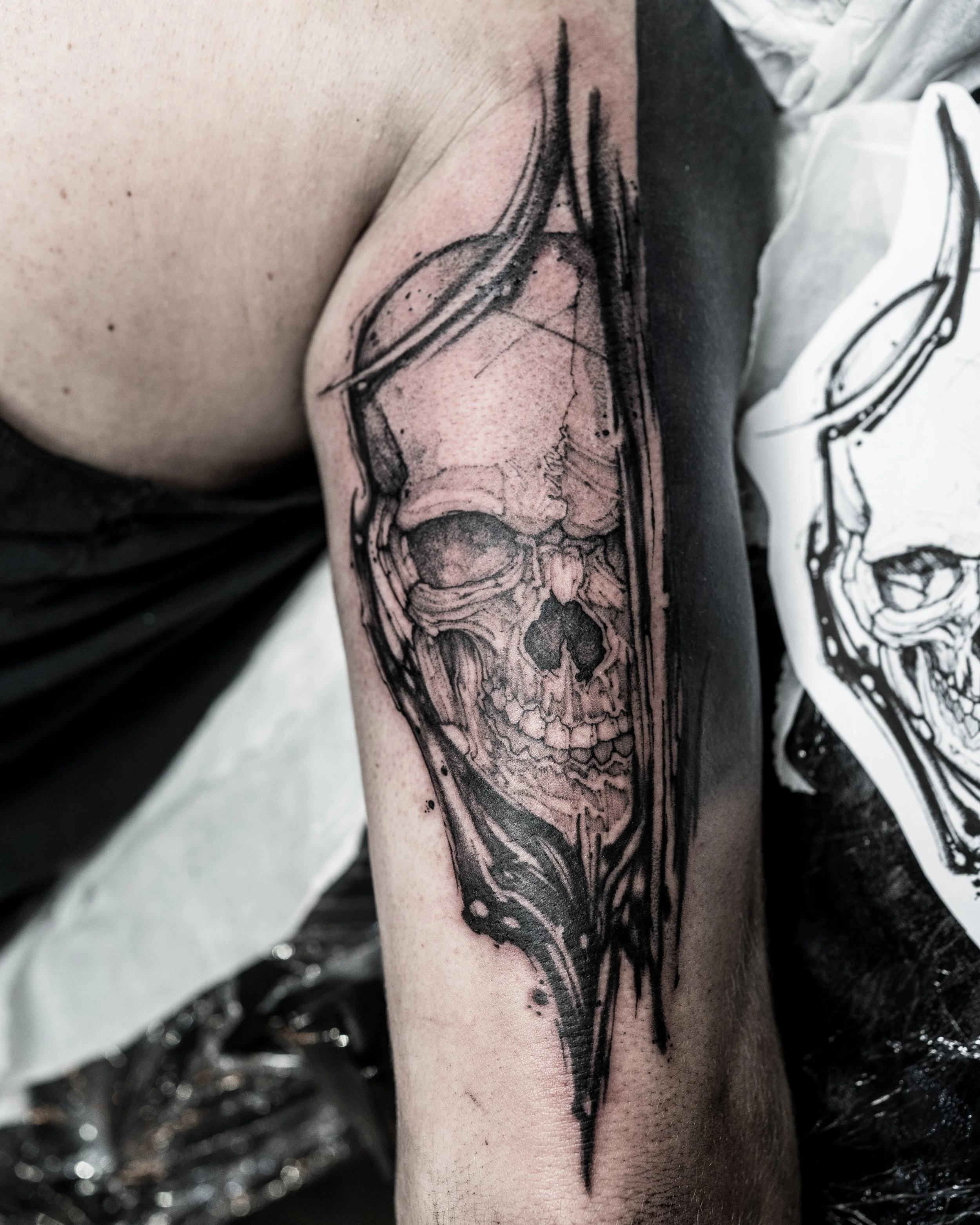 Black ink tattoo of a human skull inside a black flow frame on upper arm by Jay C Tattoo, Brighton and Hove tattoo artist, UK
