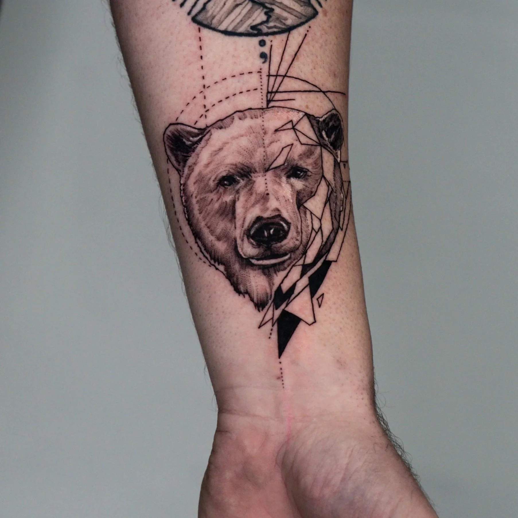 Tattoo of a bear's face with geometric and abstract elements on a person's arm done by a tattoo artist in Brighton