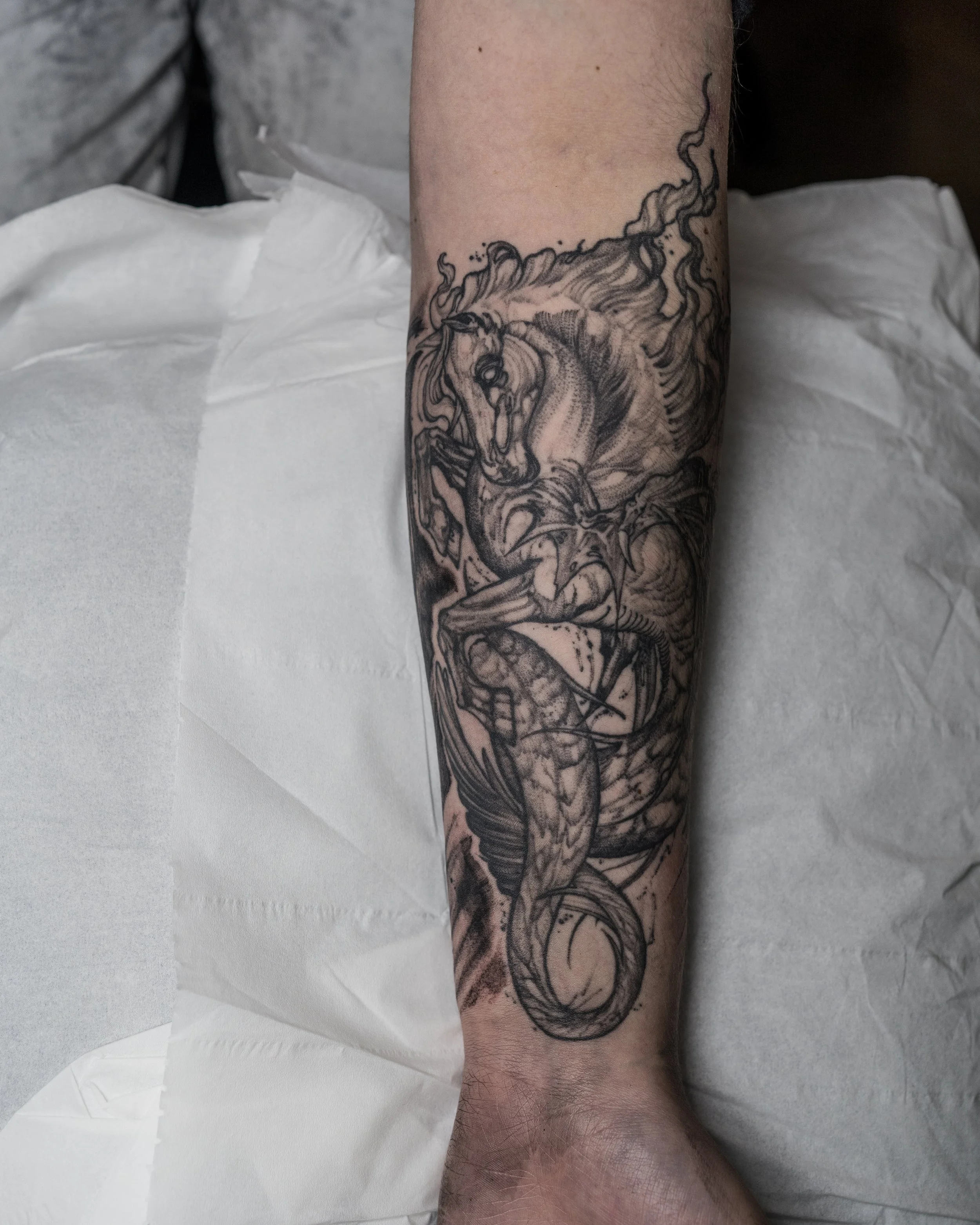 Black and gray tattoo of a hippocampus horse with wings and a long tail.