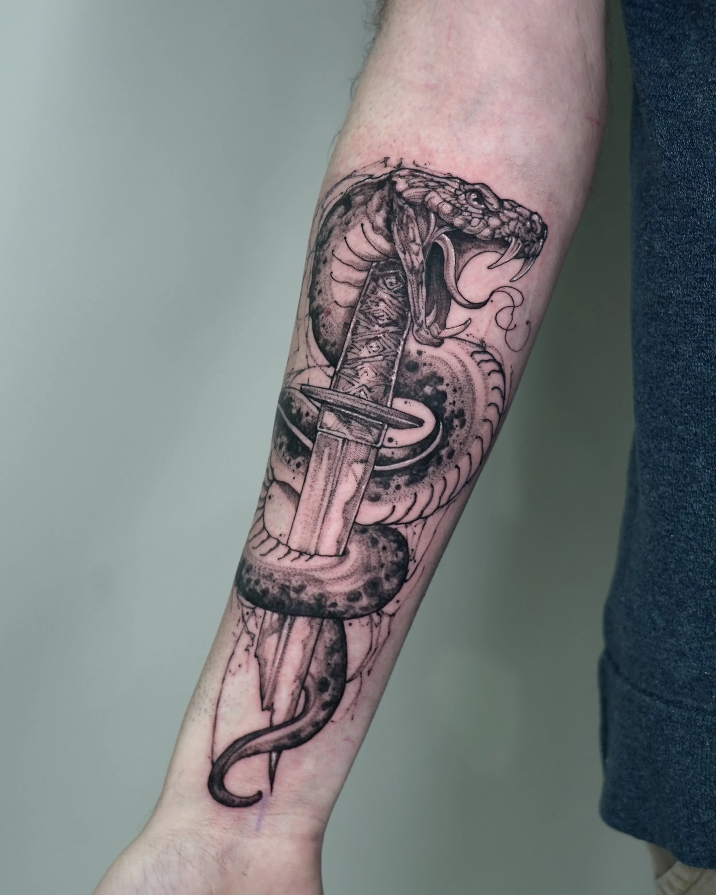 Black and grey tattoo of a snake coiled around a dagger on arm by Jay C Tattoo, tattoo artist in Brighton and Hove, UK