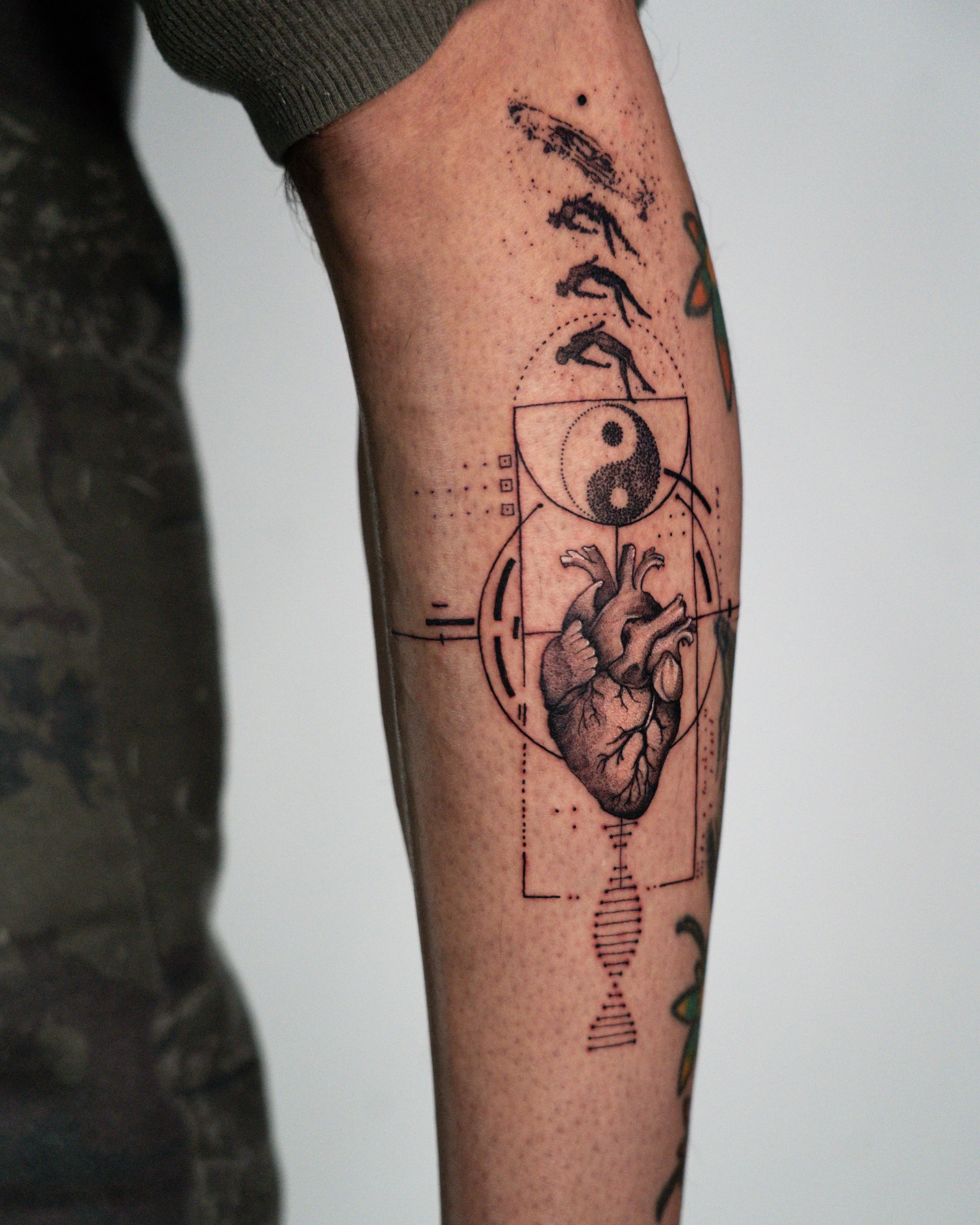 Tattoo of a detailed anatomical heart and a yin-yang symbol on a person's upper thigh, with geometric lines and shapes surrounding it.