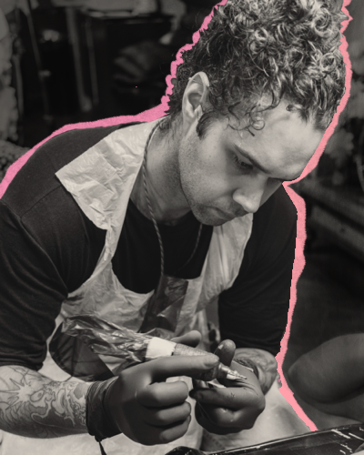 Jay C Tattoo, UK tattoo artist with curly hair, tattooing in a Brighton studio, pink accents.