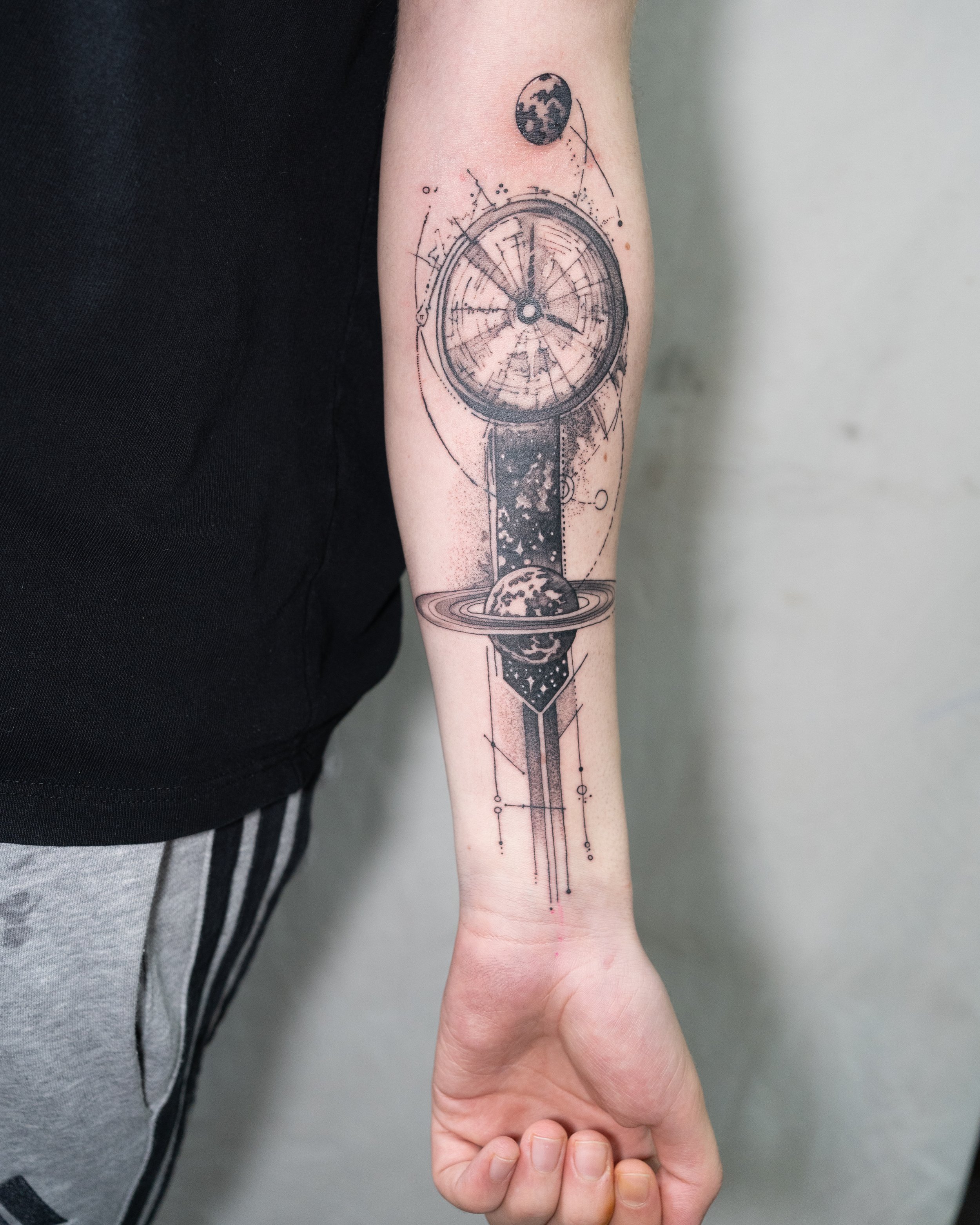 Black and grey tattoo of a cosmic clock with planetary elements on forearm by Jay C Tattoo, Brighton tattoo artist, UK
