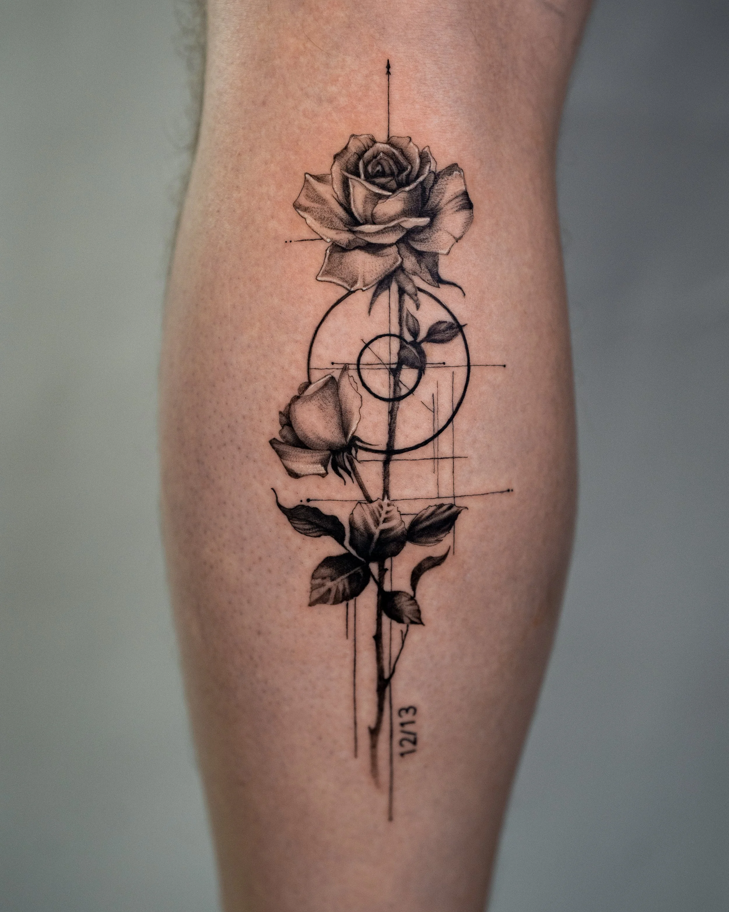 Tattoo of a rose with geometric lines and circles, along with a date '12/21/13' on a person's arm.