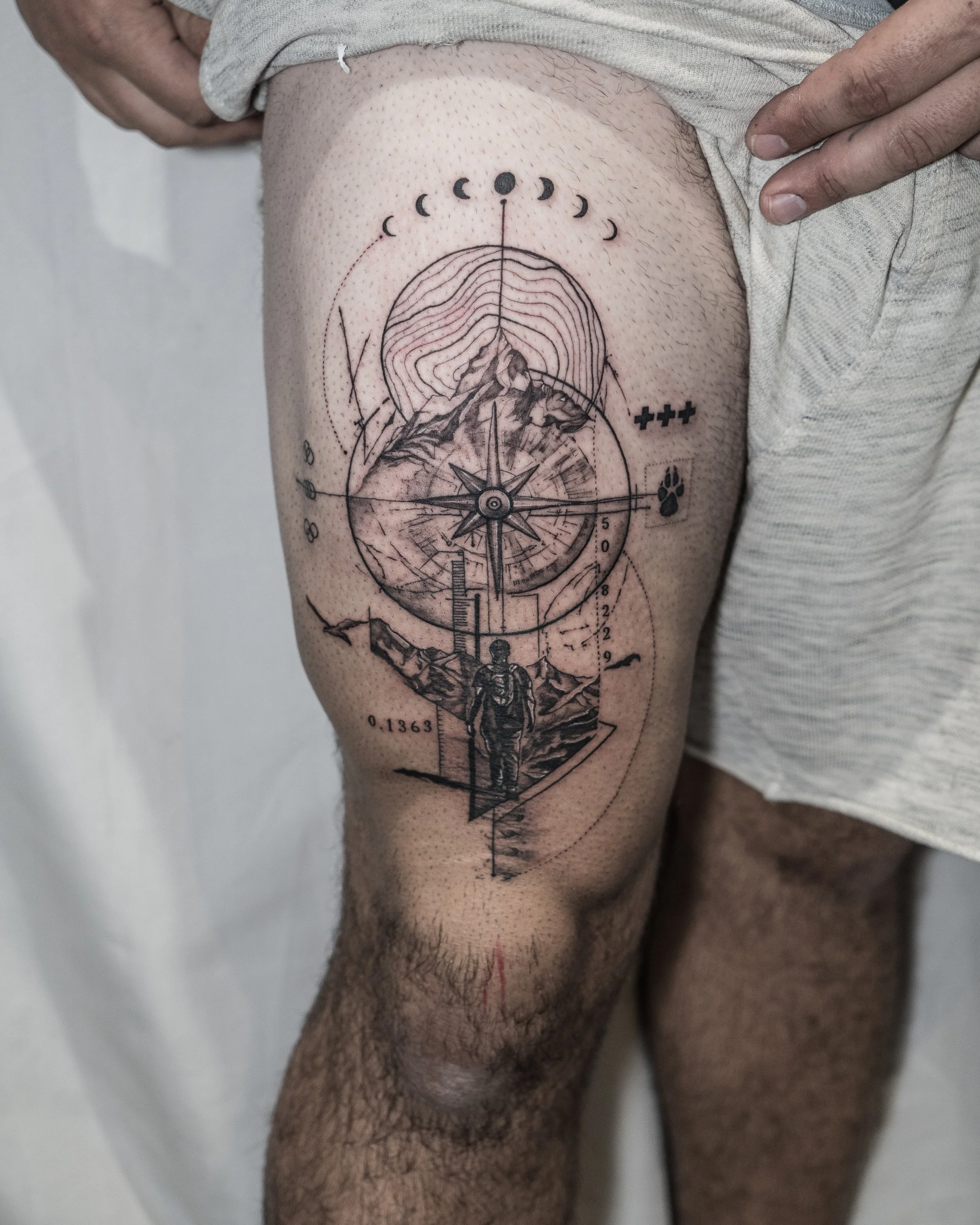 Large black line thigh tattoo featuring mountains, compass, hiker and symbolic elements by Jay C Tattoo, Brighton and Hove tattoo artist, UK

