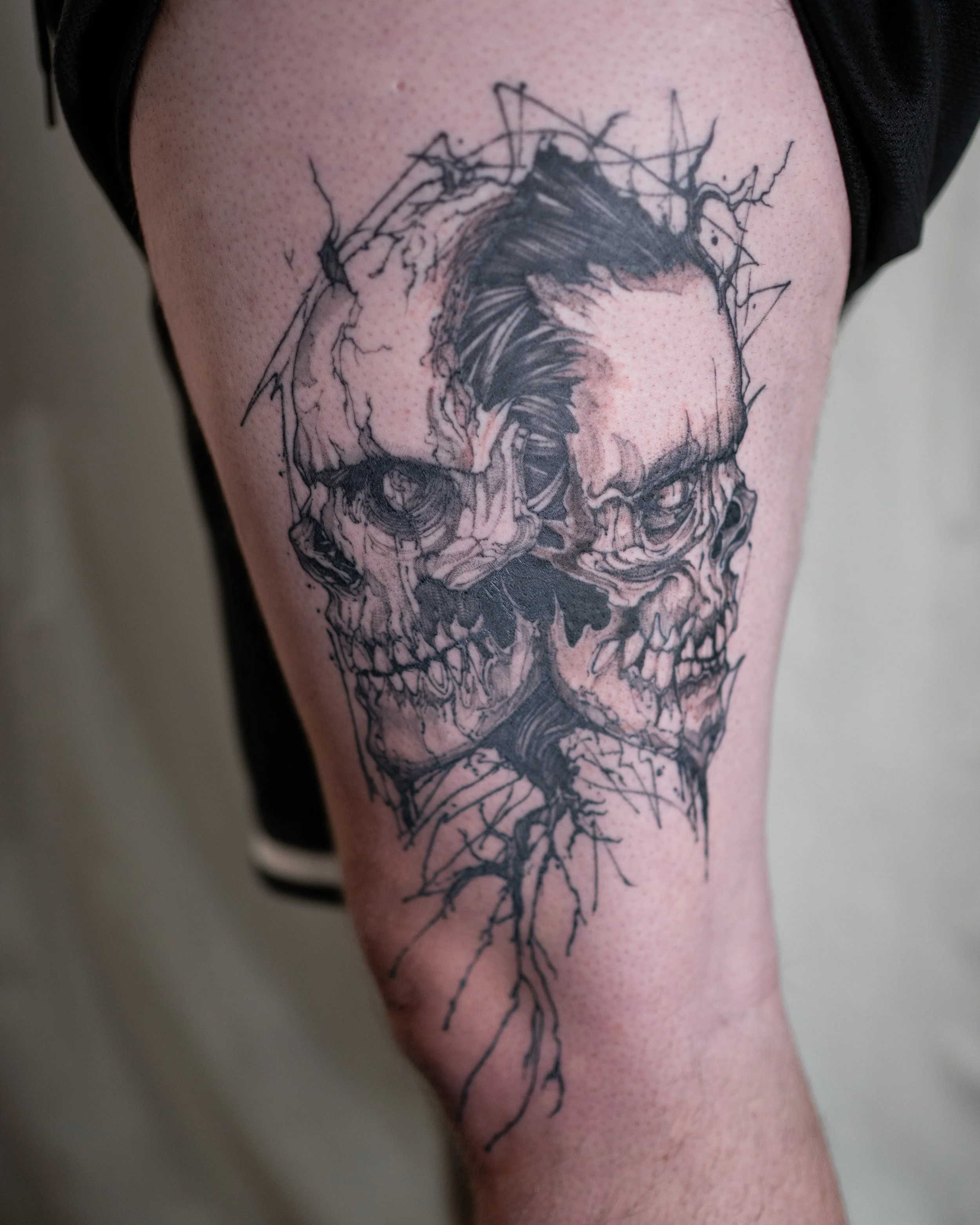 Black and grey tattoo of a Gemini skull with human face and roots on thigh by Jay C Tattoo, Brighton tattoo artist, UK
