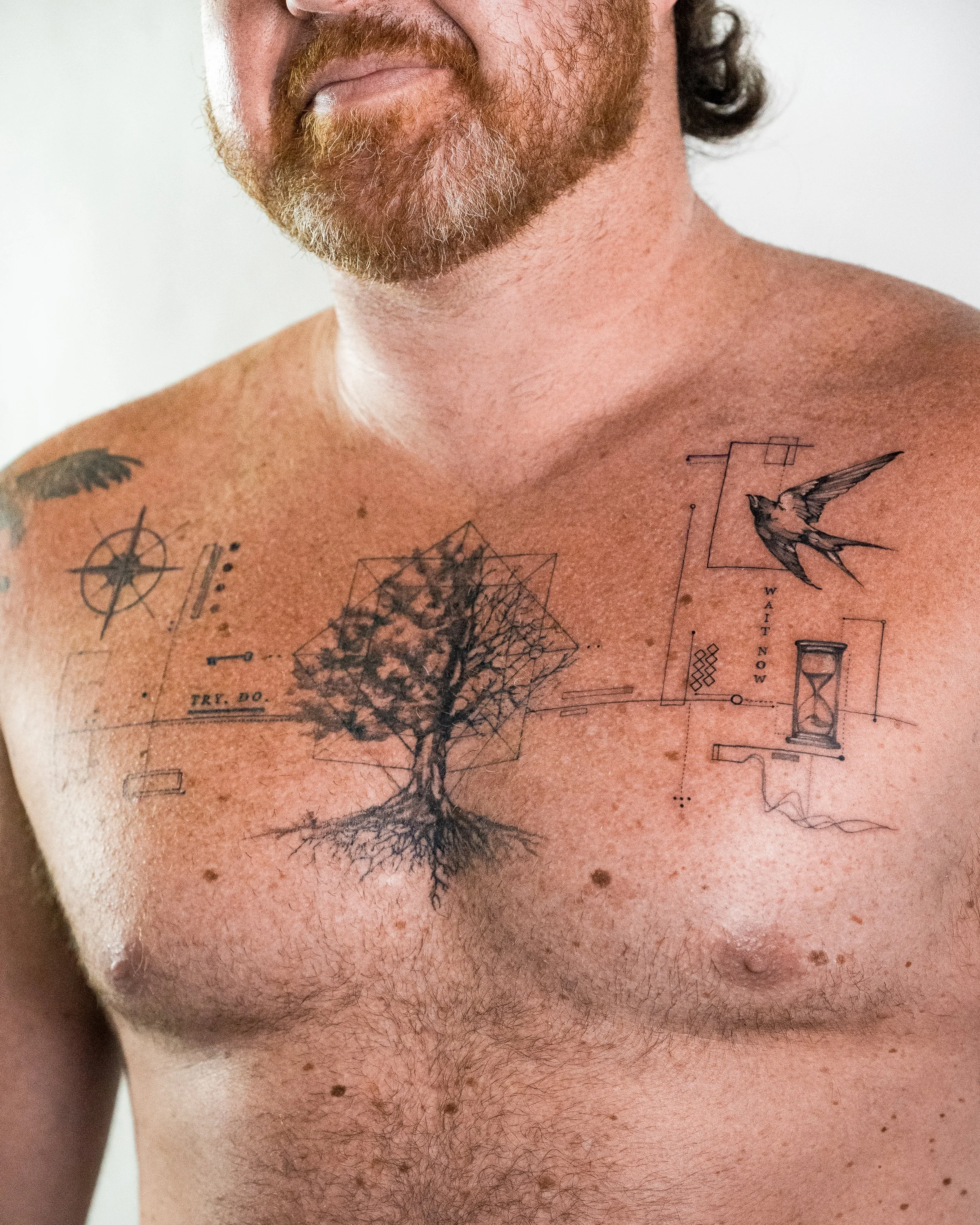 Close-up of a man's chest and neck showing tattoos, beard, and chest hair.