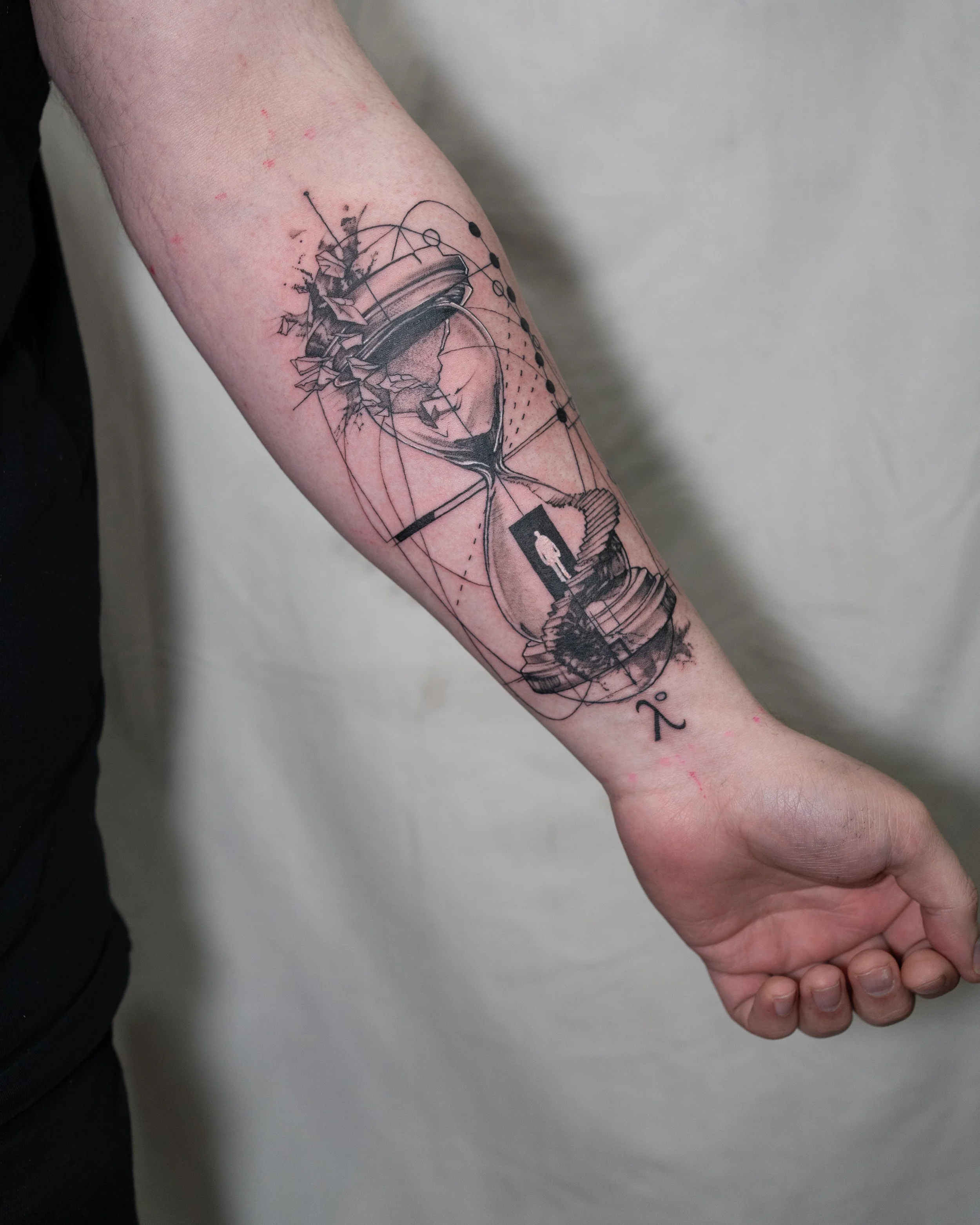 Black and grey micro realism hourglass tattoo with geometric details and small figure on forearm by Jay C Tattoo, Brighton tattoo artist, UK