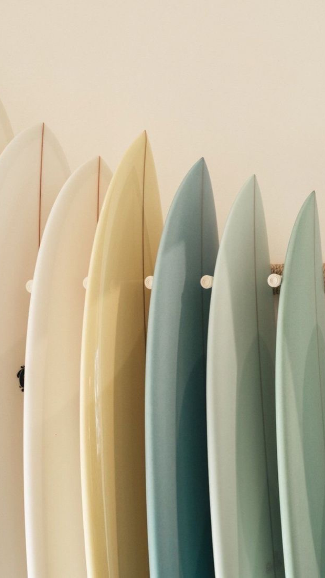 A row of colorful surfboards standing upright against a beige wall.