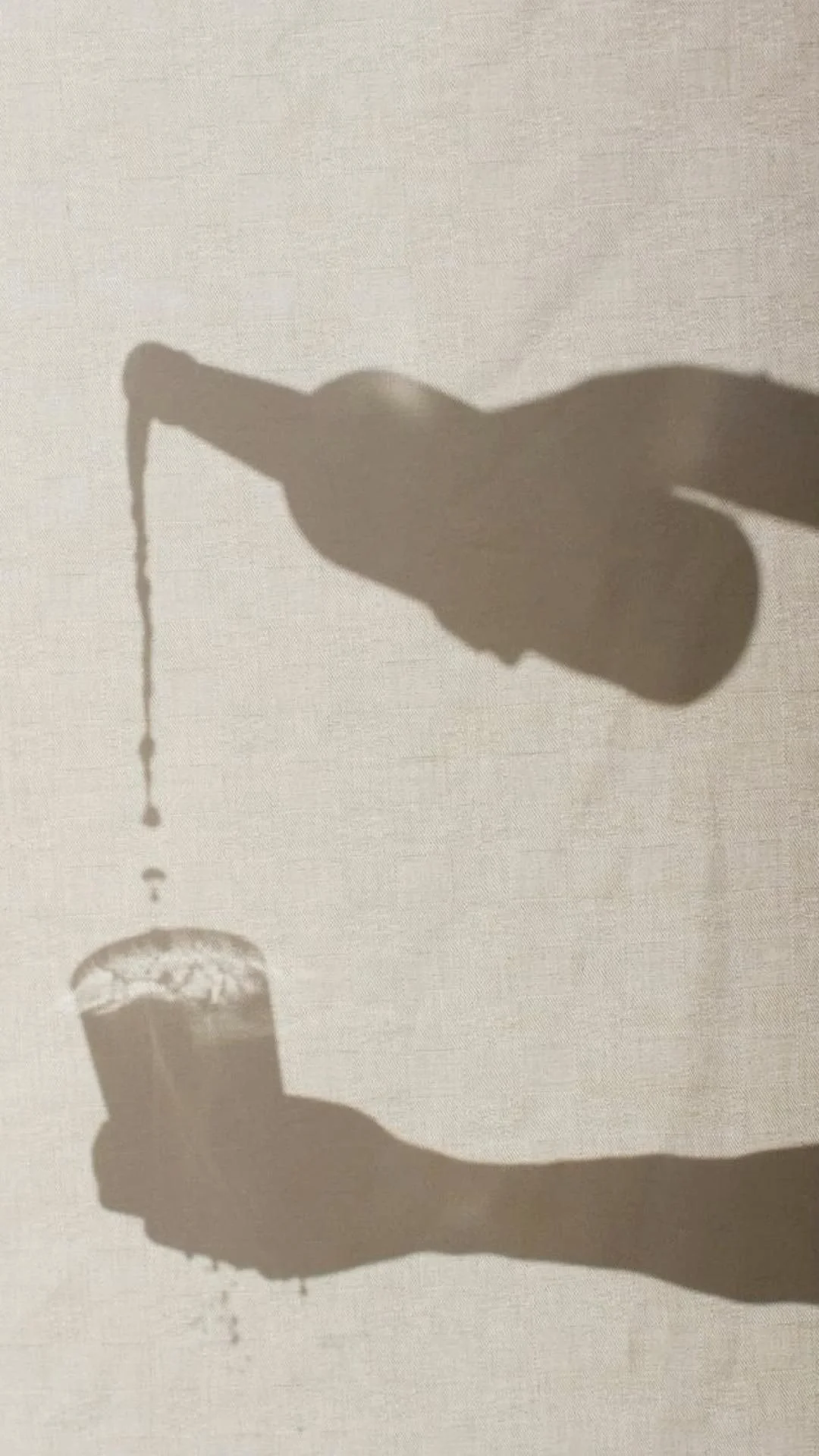 Shadow of a person pouring water from a bottle into a glass on a plain background.