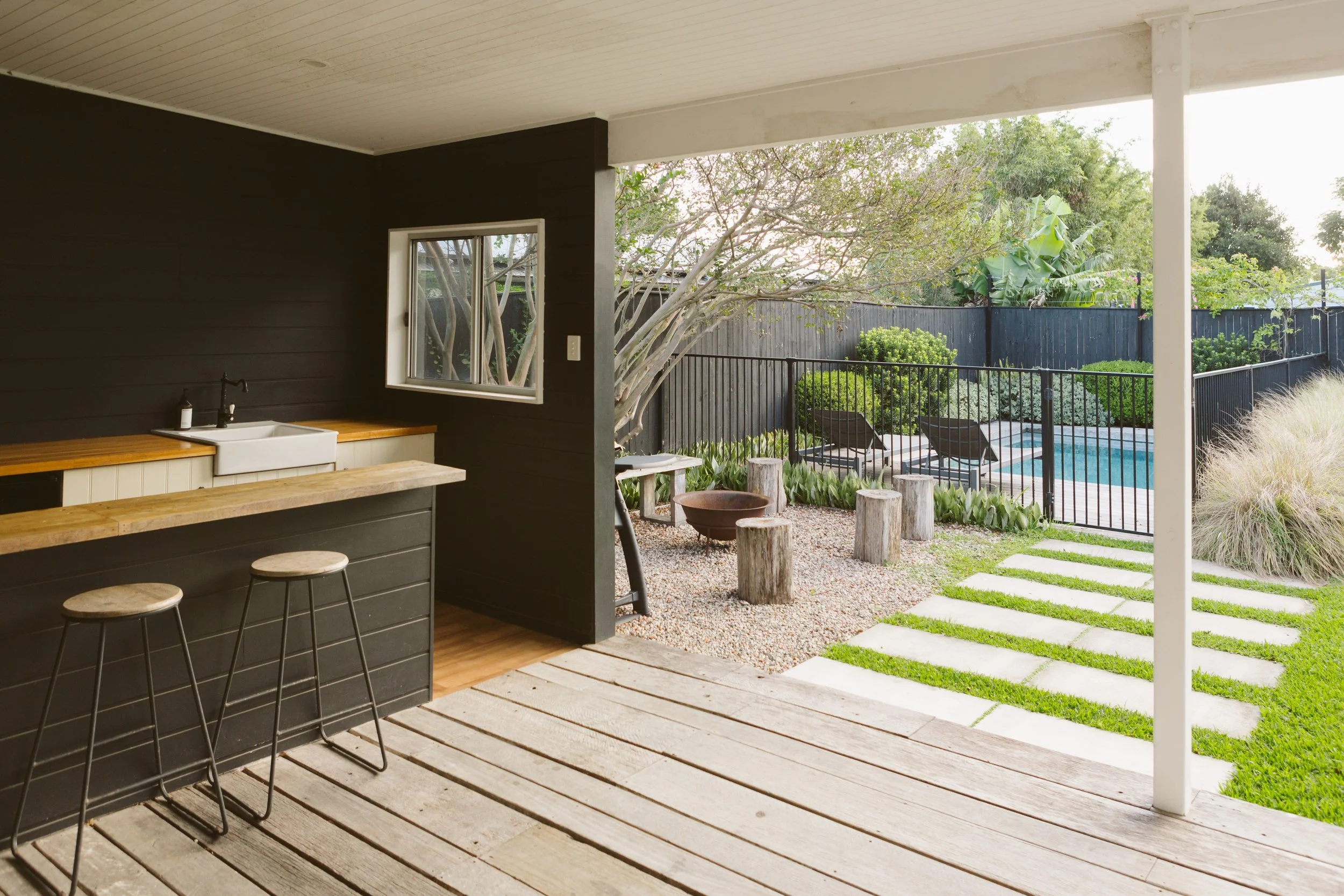 View from a covered patio overlooking a backyard with a swimming pool, lounge chairs, and greenery, including trees and shrubs.