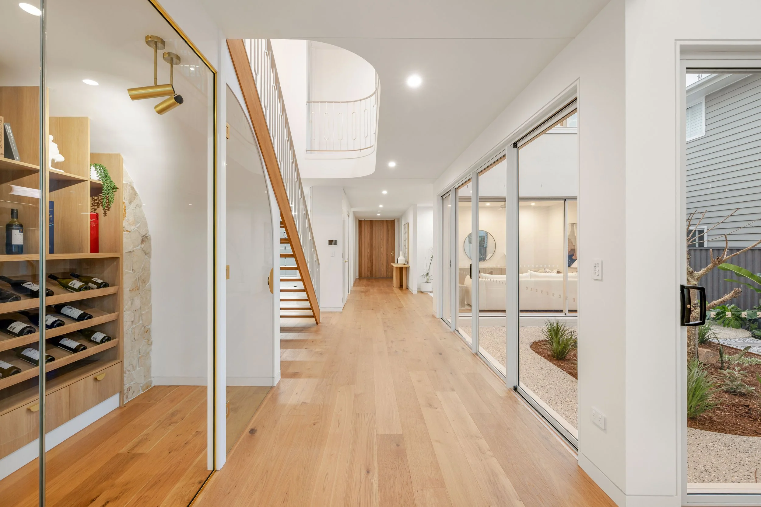 Bright modern interior with wooden floors, staircase, and large sliding glass doors leading to an outdoor garden area.
