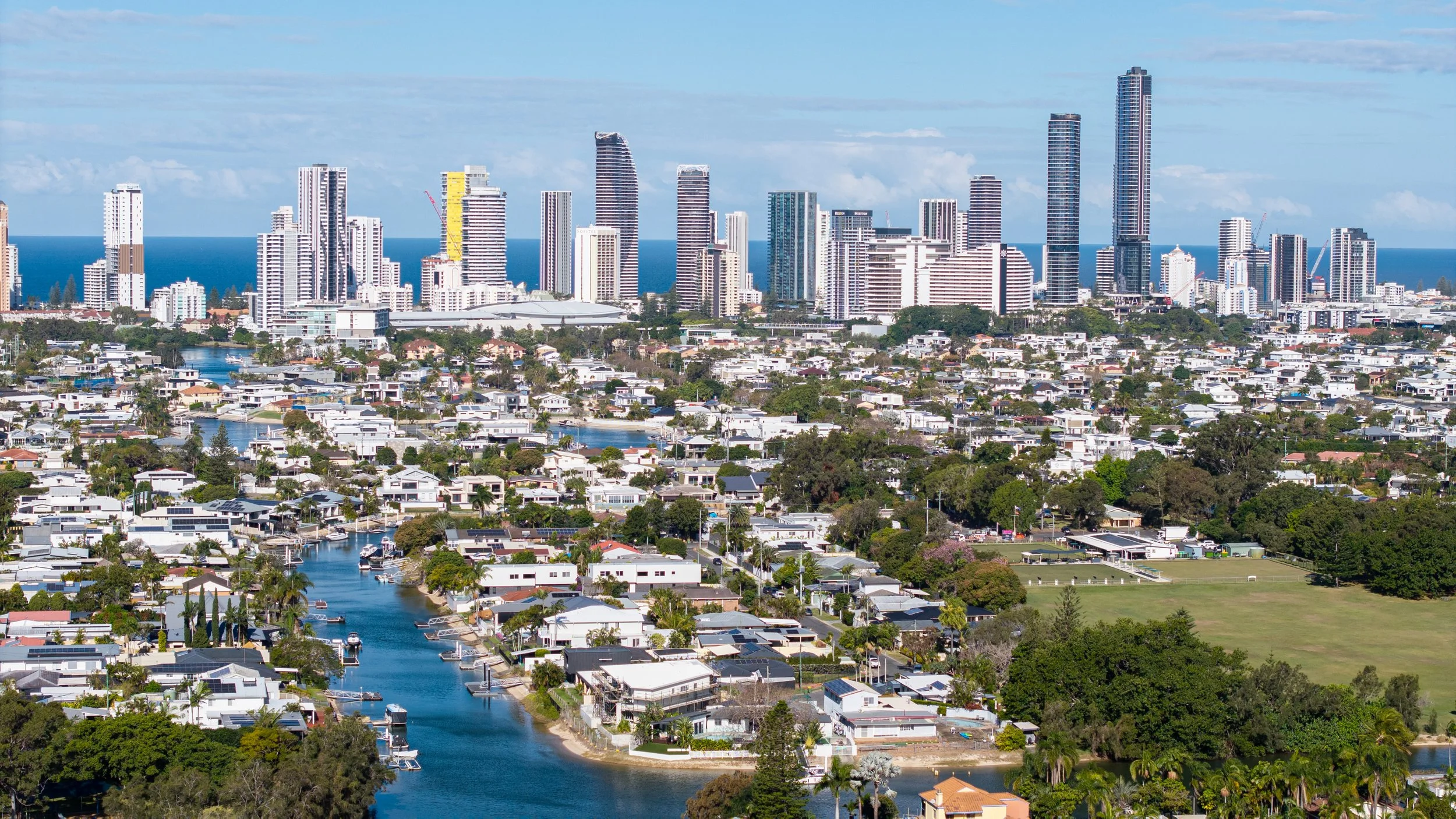 Aerial view of a city with high-rise buildings, water bodies, and residential houses, with the ocean visible in the background.