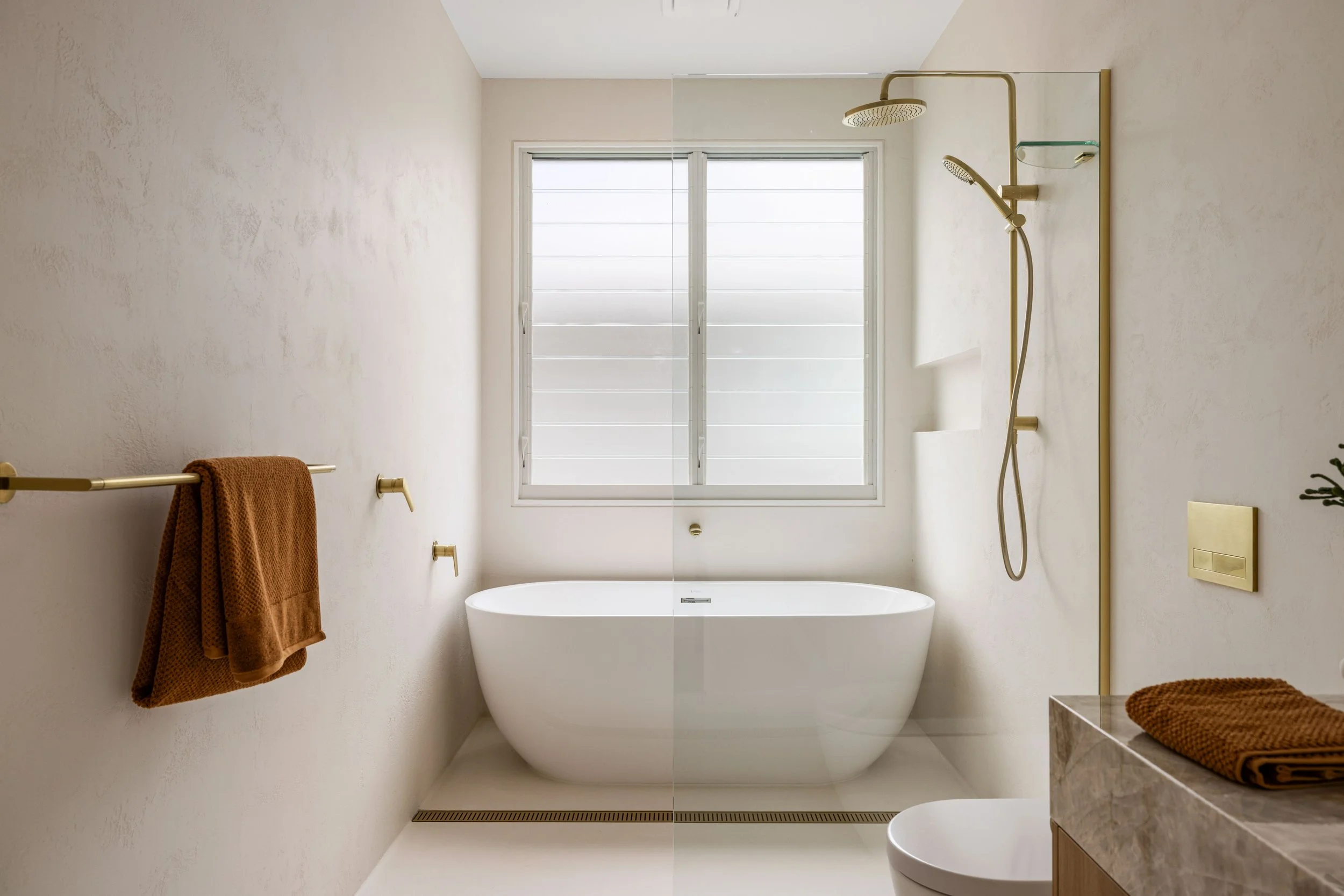 Modern bathroom with a bathtub under a window, and a shower with a gold showerhead on the wall.