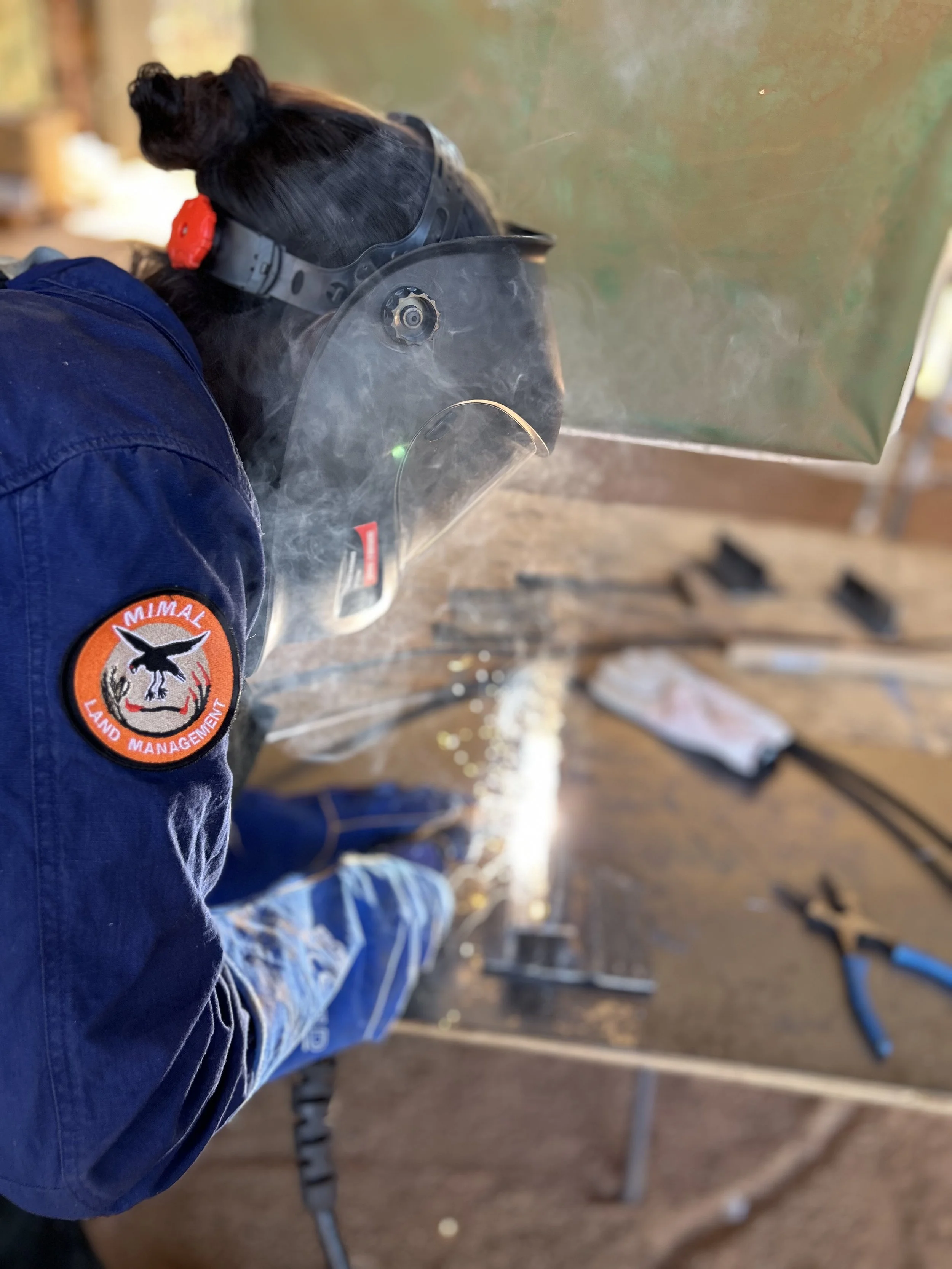 Female ranger in protective mask and gloves welding steel as part of hands-on training on Country.