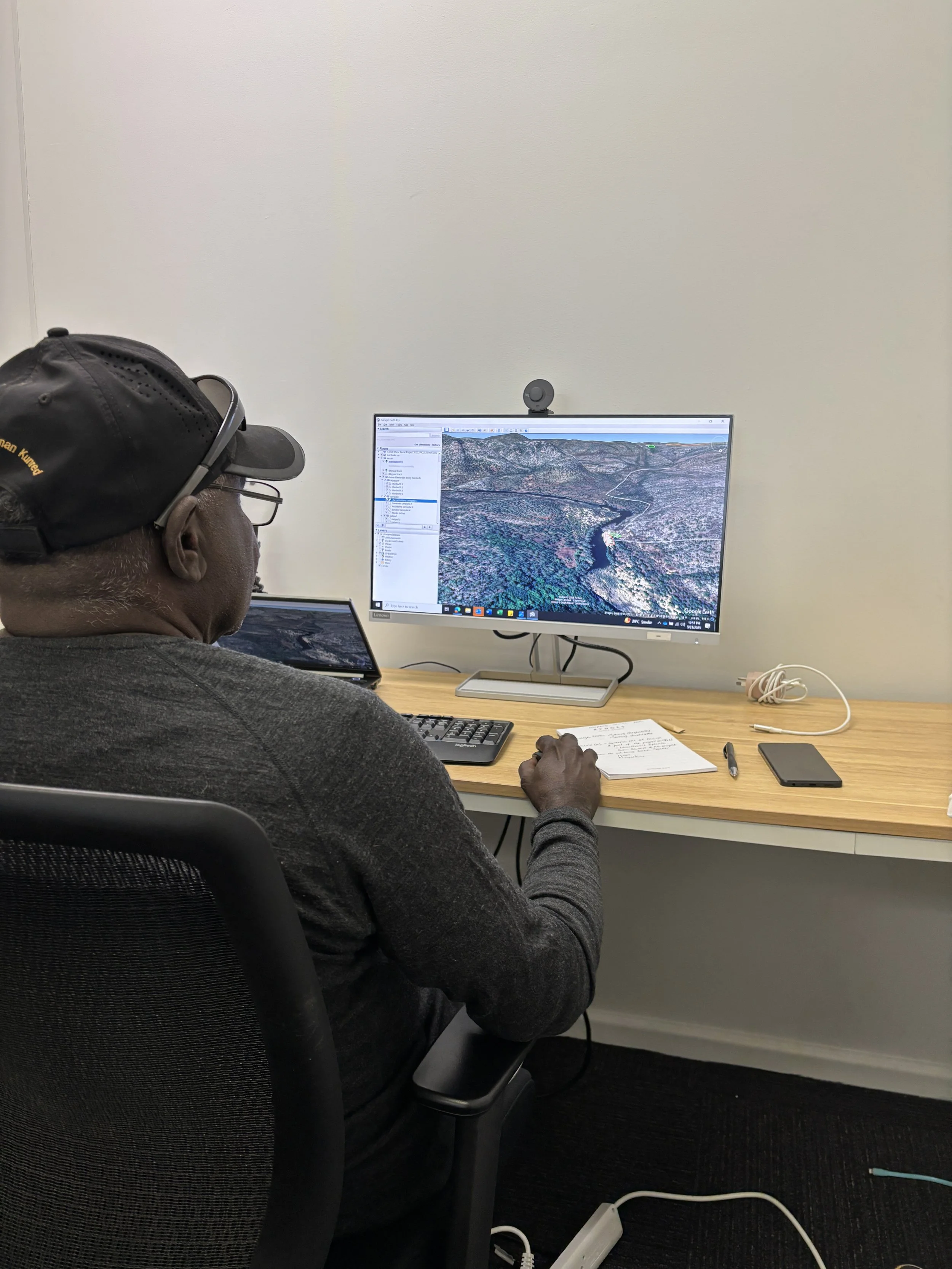 Male ranger sitting at desk, looking at Country on Google Earth on Desktop screen.