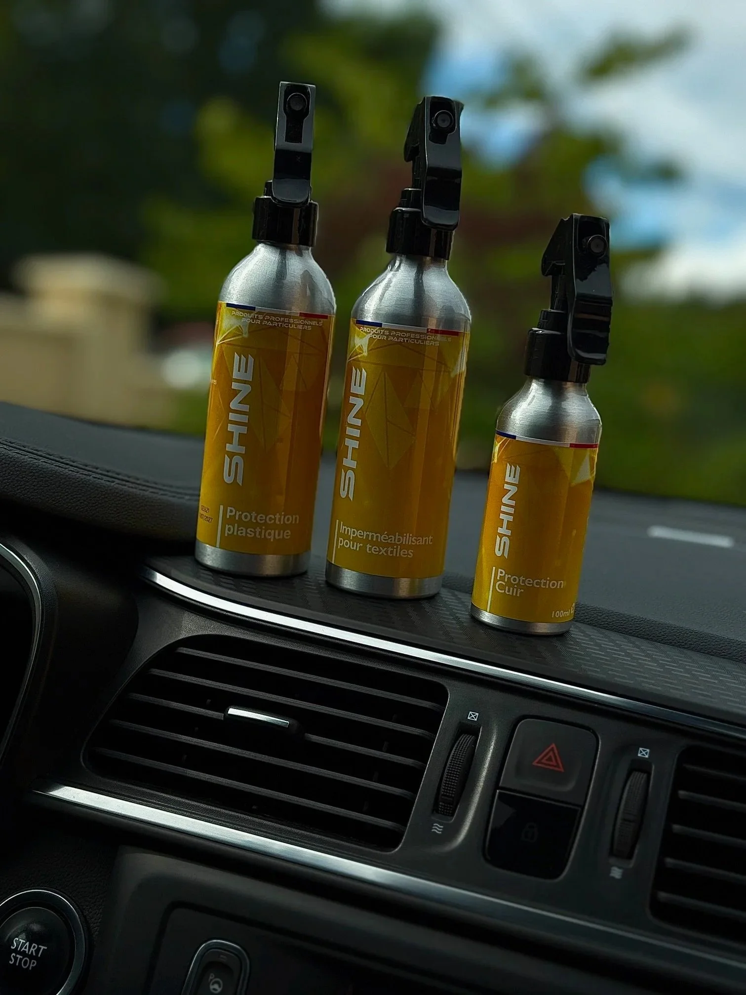 Trois bouteilles de produit de nettoyage Shine sur le tableau de bord d'une voiture, utilisées pour la protection de plastique, le traitement imperméabilisant pour textiles, et la protection du cuir.
