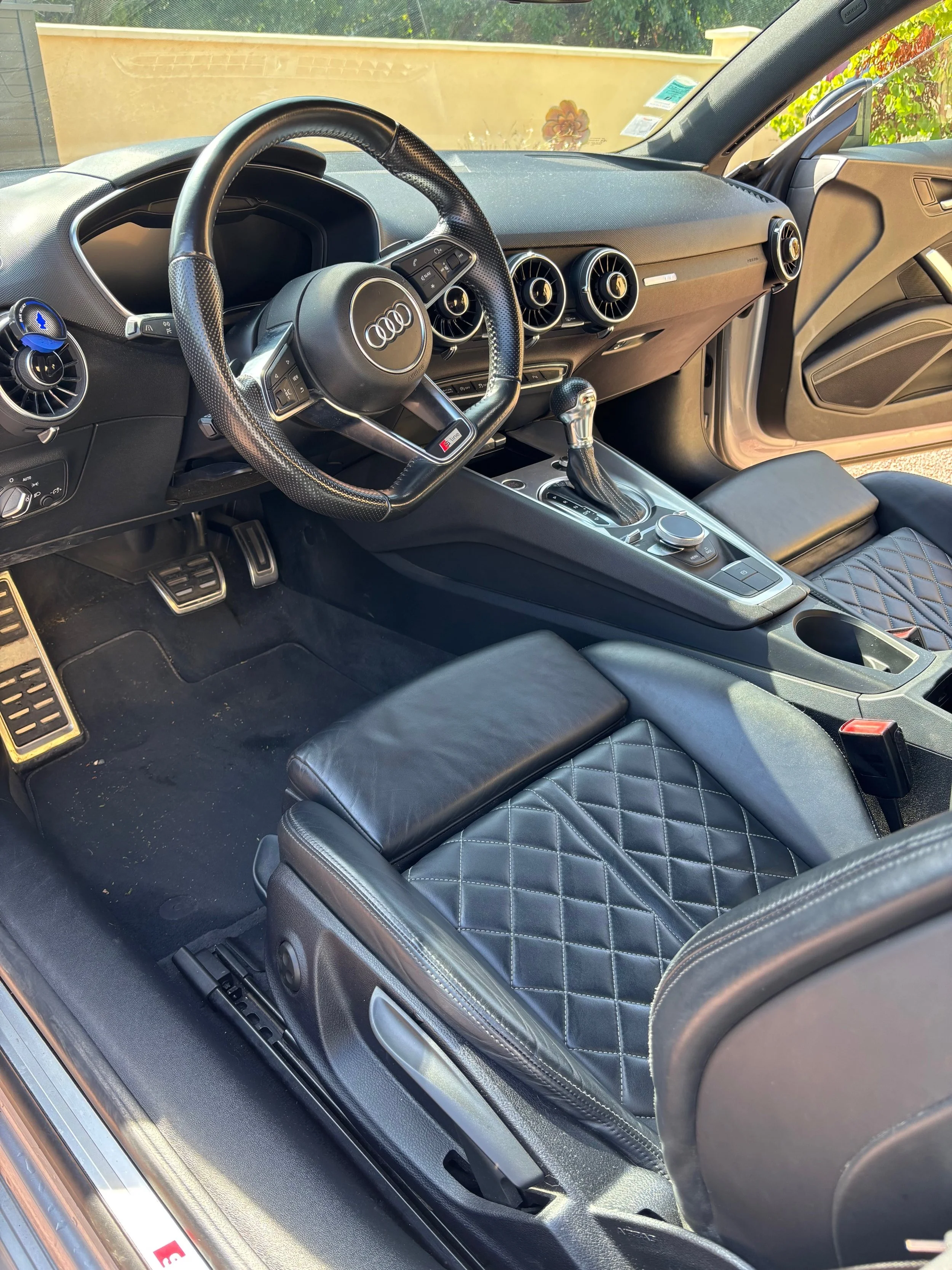 Intérieur d'une voiture Audi noire avec un volant, un levier de vitesse, des sièges en cuir noir avec motif capitonné, et un tableau de bord.