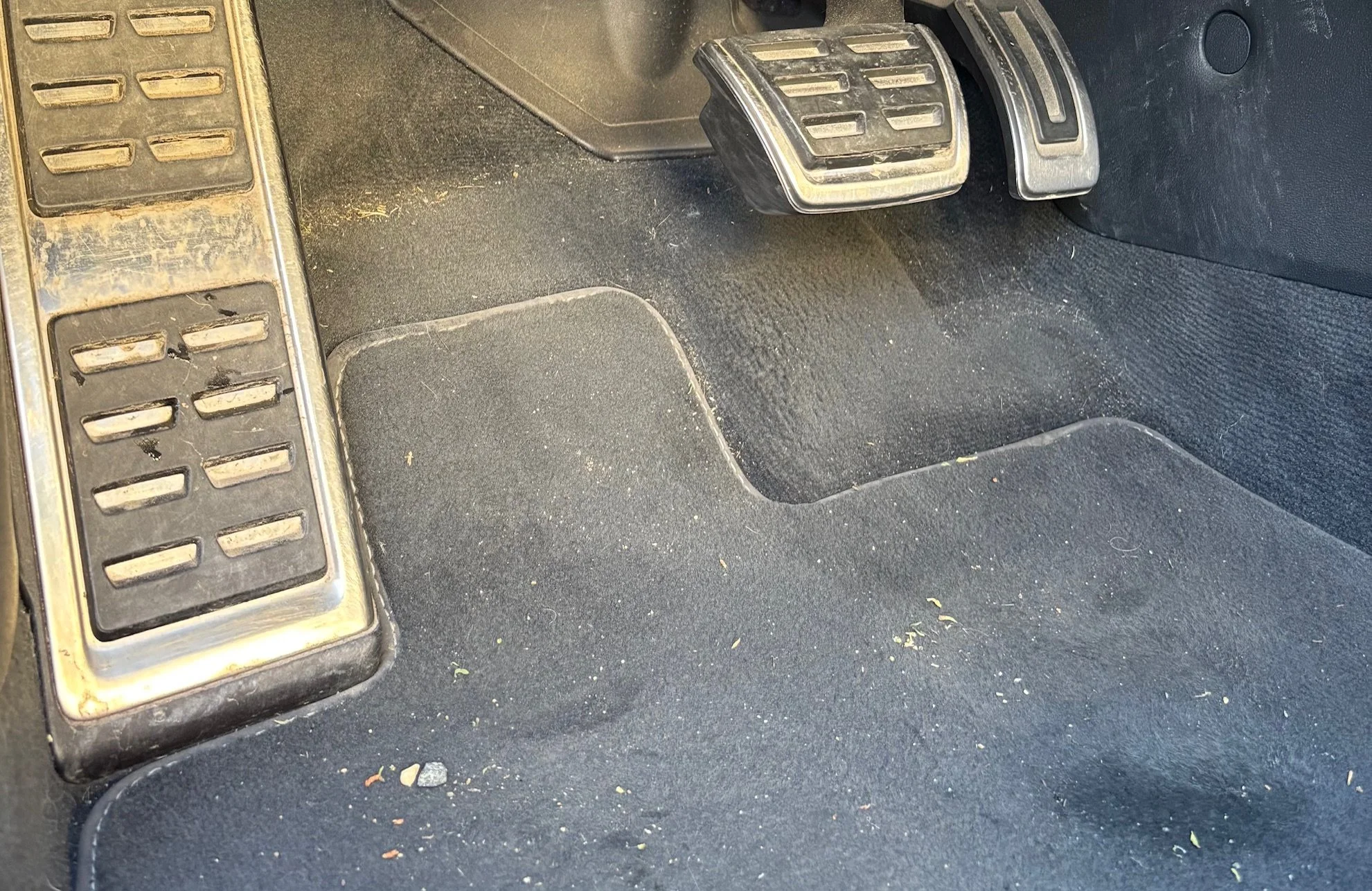 Intérieur de voiture montrant les pédales d'accélérateur, de frein et d'embrayage, ainsi que le tapis de sol sale.