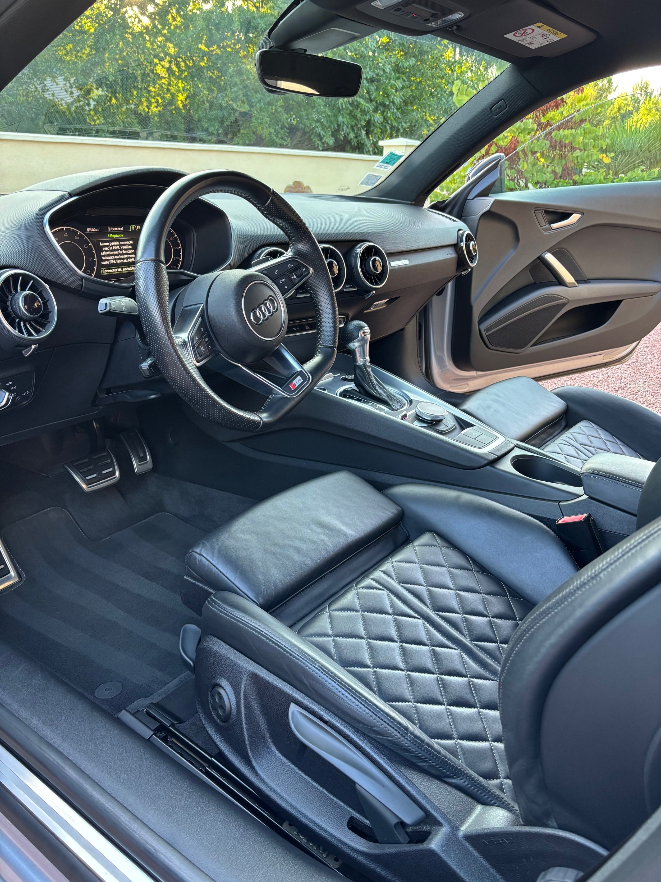 Intérieur d'une voiture, vue du conducteur avec un volant, tableau de bord, levier de vitesse, sièges en cuir avec motif quilté.
