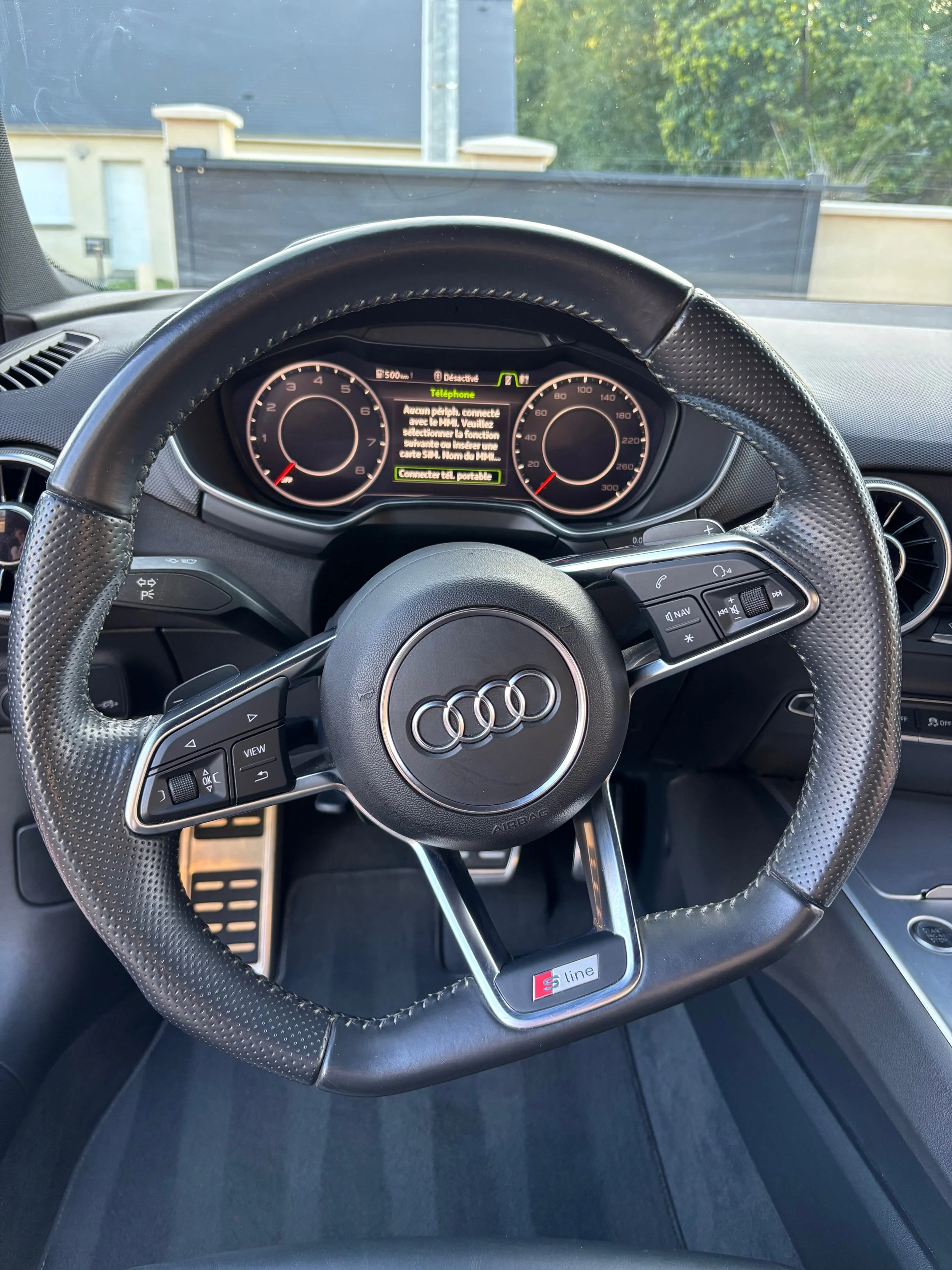 Tableau de bord d'une voiture Audi avec un volant sport S line, affichage numérique, et un écran central.