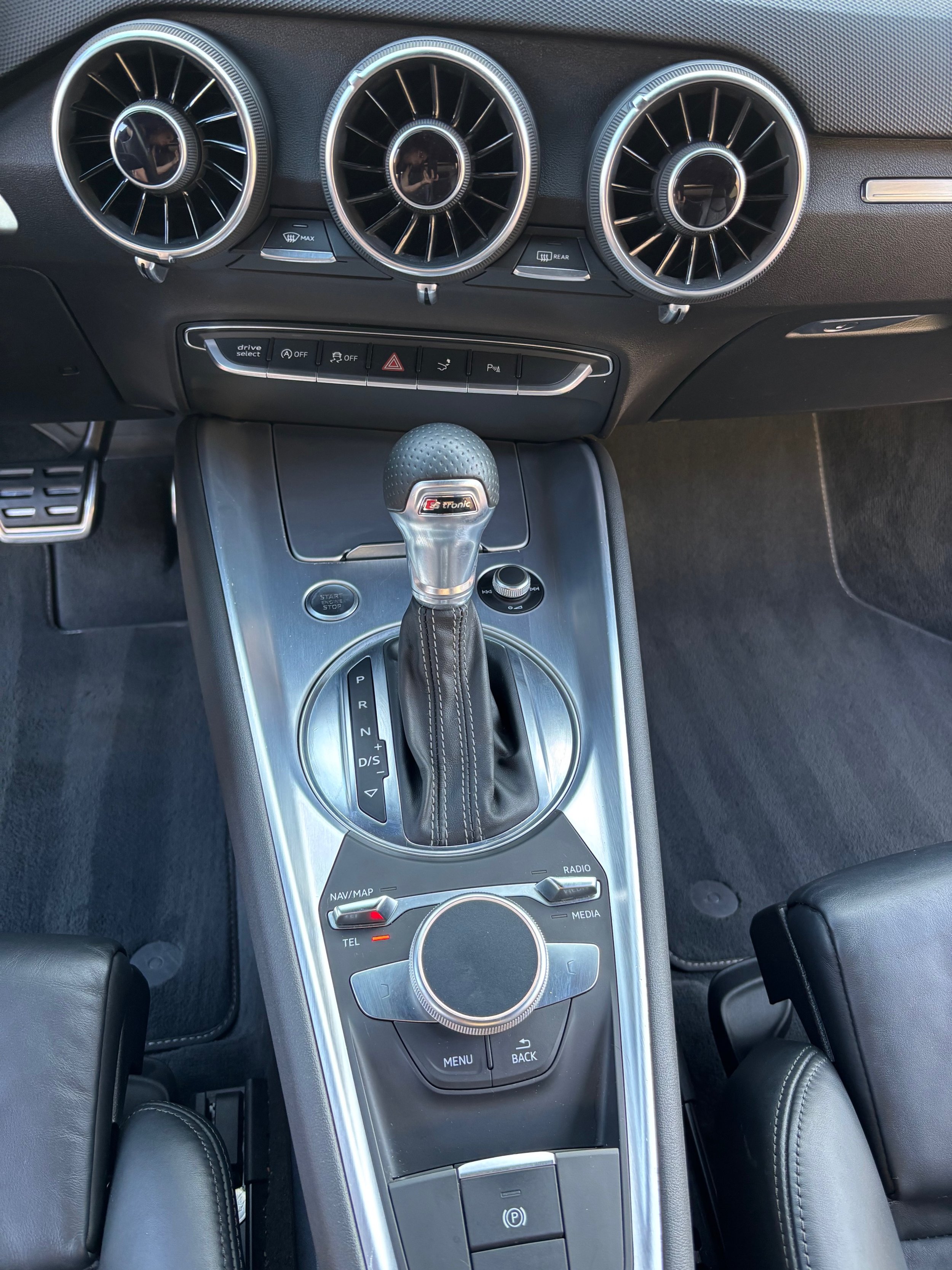 Intérieur d'une voiture de luxe, vue de haut, avec un tableau de bord moderne, un levier de vitesse, contrôles de navigation, radio, médias, et un bouton de stationnement électronique.