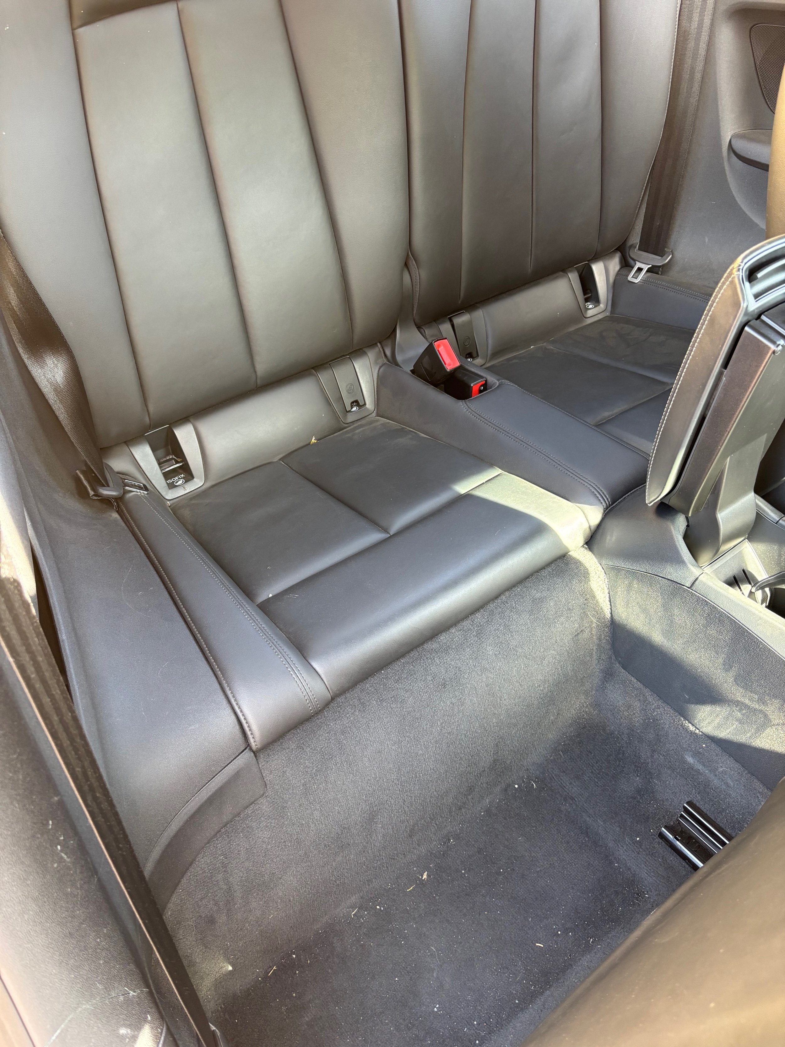Intérieur d'une voiture montrant la banquette arrière en cuir noir avec des ceintures de sécurité et un sol en tapis noir.