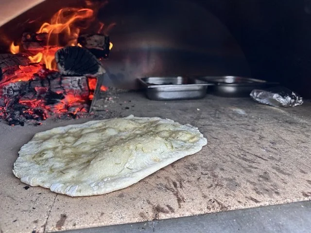 Flatbread baking inside a wood-fired oven with glowing embers and fire visible in the background.