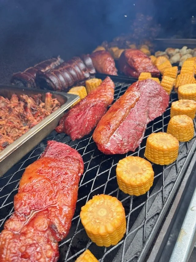 Meat and corn on a grill, with a tray of shredded meat in the background.