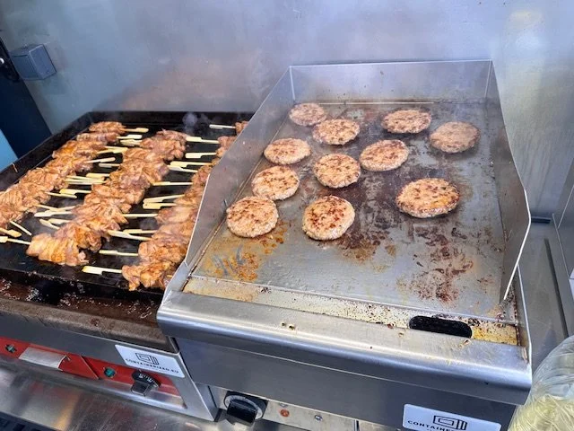 Spiesjes met vlees en hamburgers die worden gegrild op een commerciële bakplaat