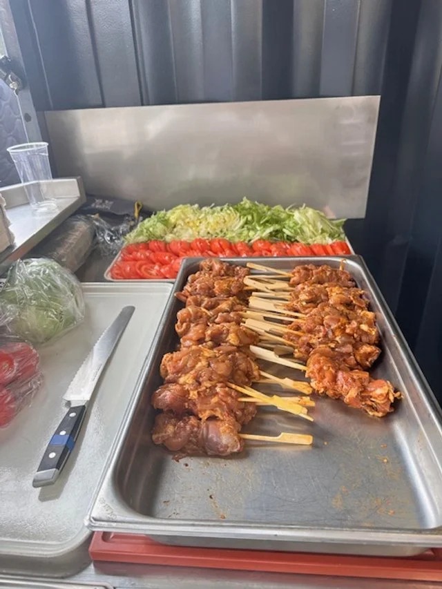 Tray of cooked chicken skewers with sliced tomatoes and chopped lettuce in the background.
