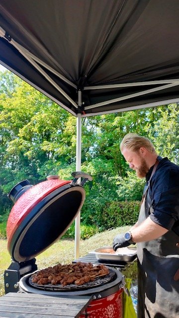 A man grilling meat on a barbecue grill under a canopy outdoors on a sunny day.
