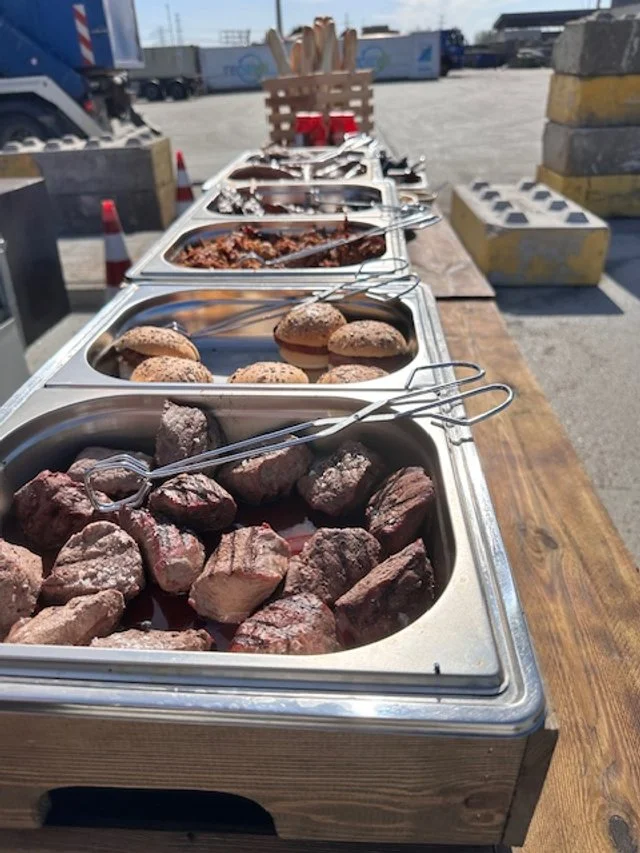 Buffet of raw meats and cooked dishes on a wooden table outdoors.