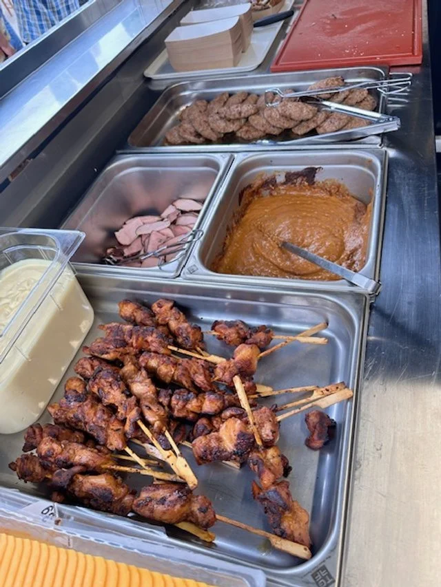 Buffet with trays of grilled chicken skewers, sliced turkey, meatloaf, cooked hamburger patties, and a container of mashed potatoes with gravy.