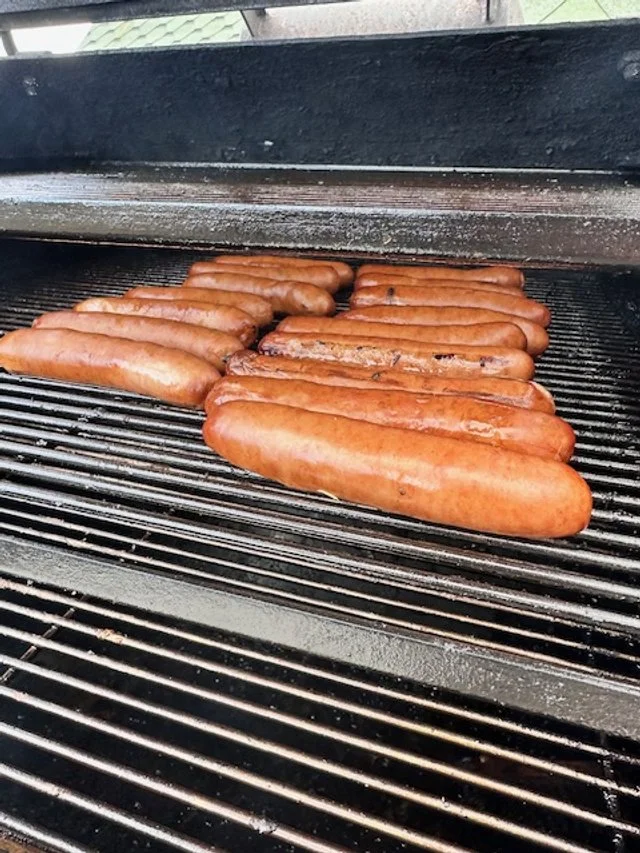 Hot dogs cooking on a barbecue grill.