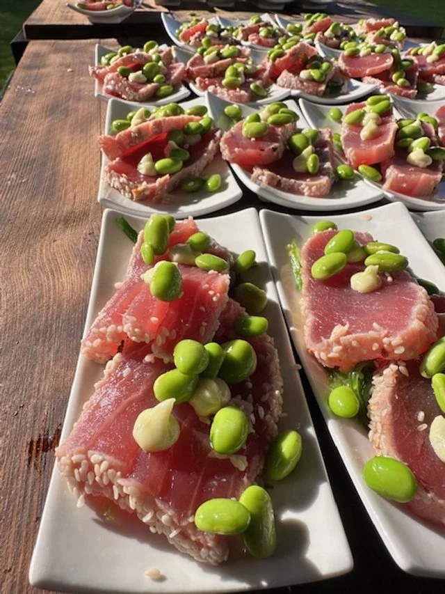 Sliced raw tuna topped with green edamame beans on small white rectangular plates.